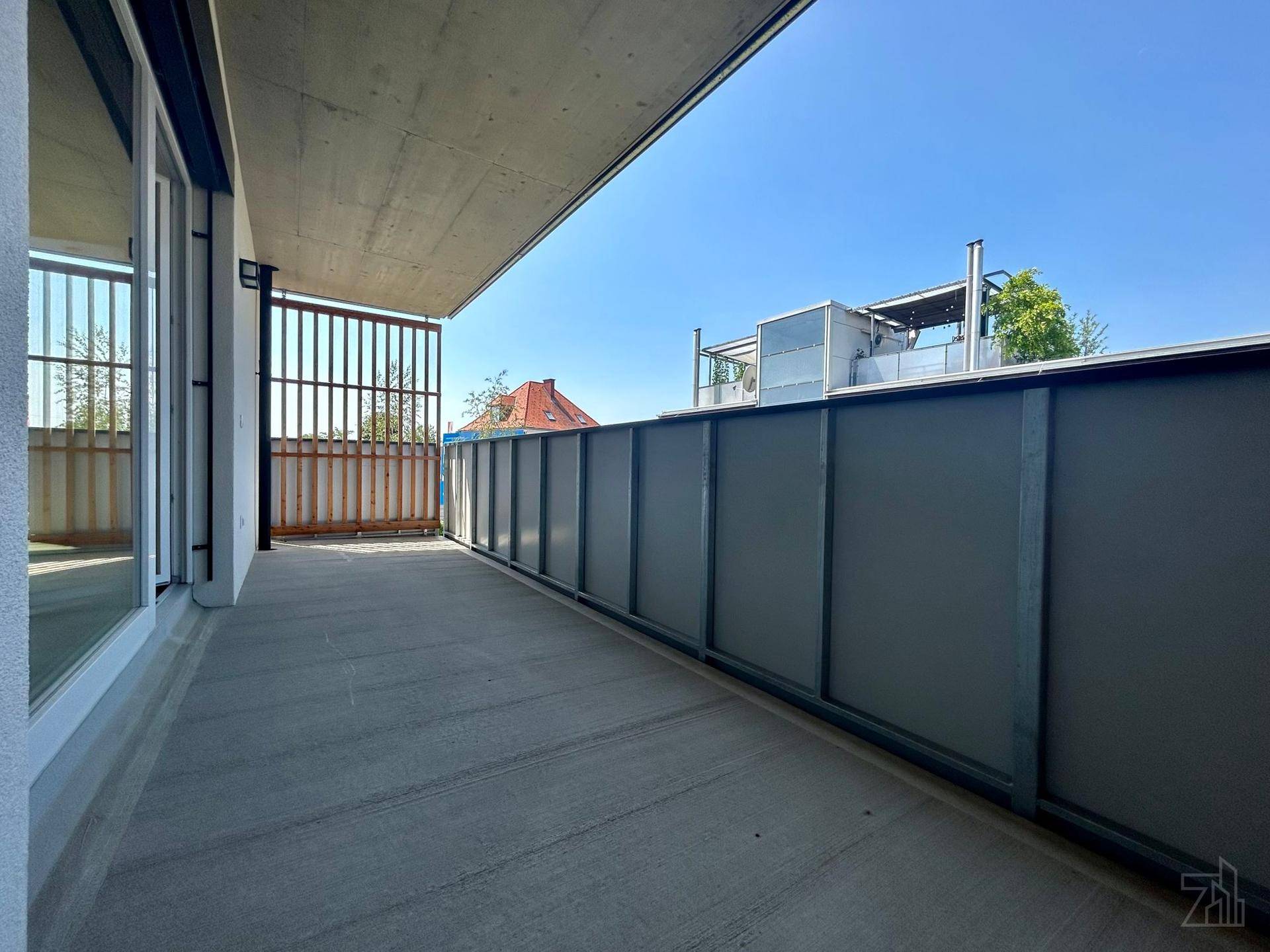 Geräumiger Balkon mit dunkler Brüstung und Blick auf die Nachbarschaft unter blauem Himmel.