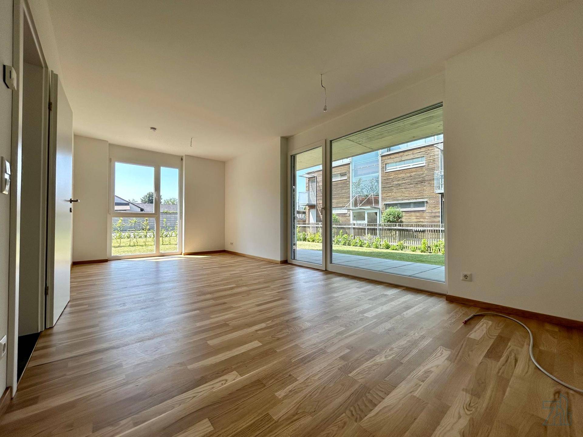 Geräumiges Wohnzimmer mit großen Fenstern, Holzboden und Blick ins Grüne.