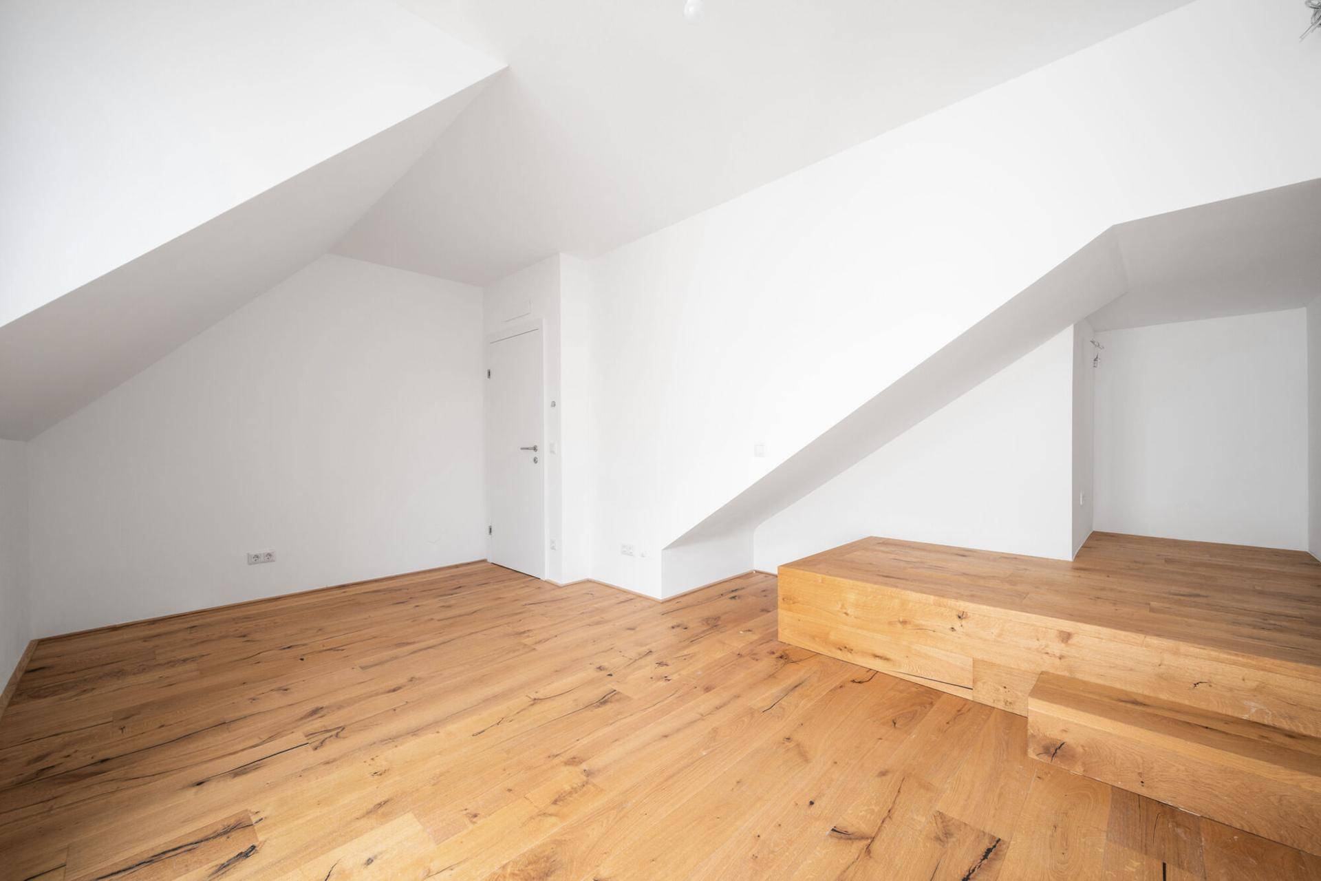 Geräumiges Dachgeschosszimmer mit Holzboden und integrierter Holzplattform.