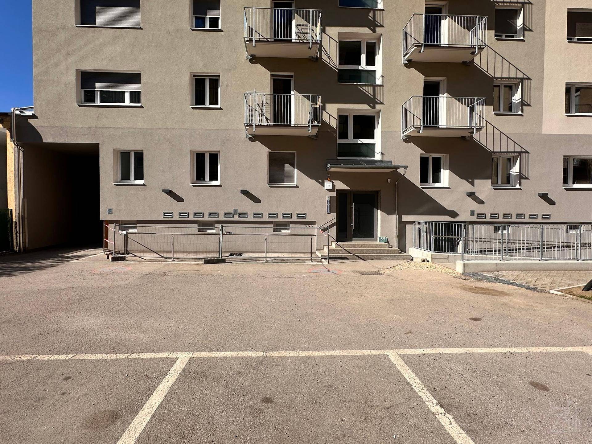 Fassade eines Wohngebäudes mit mehreren Balkonen und einem davorliegenden Parkplatz.