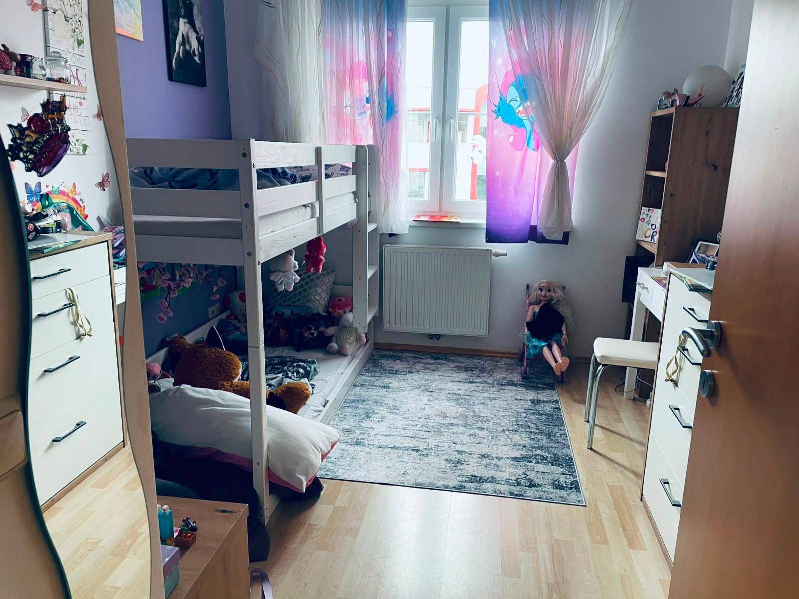 Gemütliches Kinderzimmer mit Etagenbett, Holzboden und bunten Vorhängen.