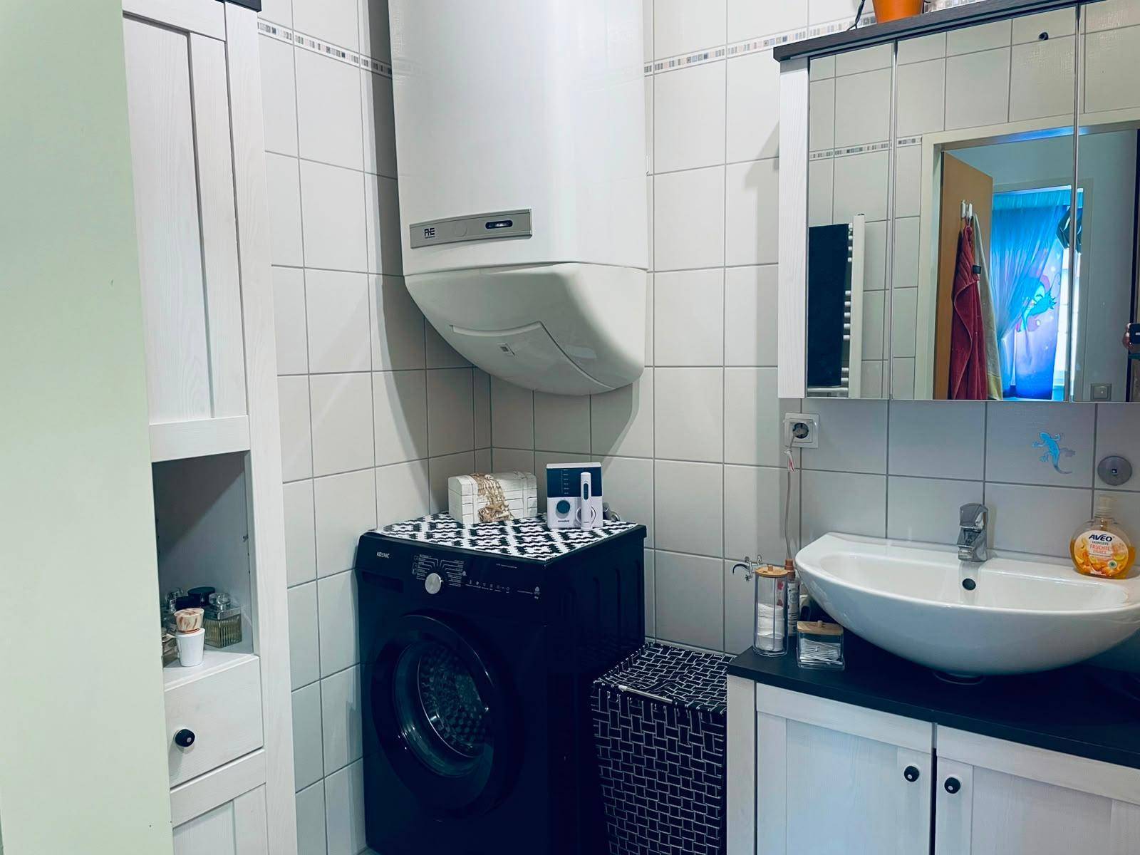 Praktisches Badezimmer mit Waschmaschine, Waschbecken und Spiegelschrank.