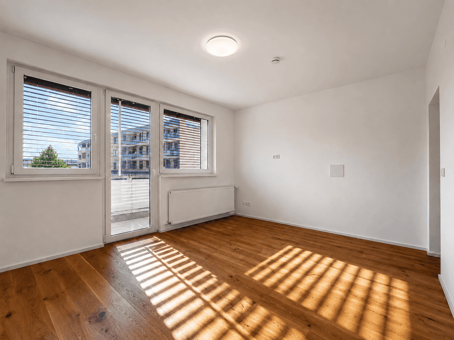 Helles Wohnzimmer mit Holzboden und Zugang zum Balkon, durchflutet von natürlichem Sonnenlicht.