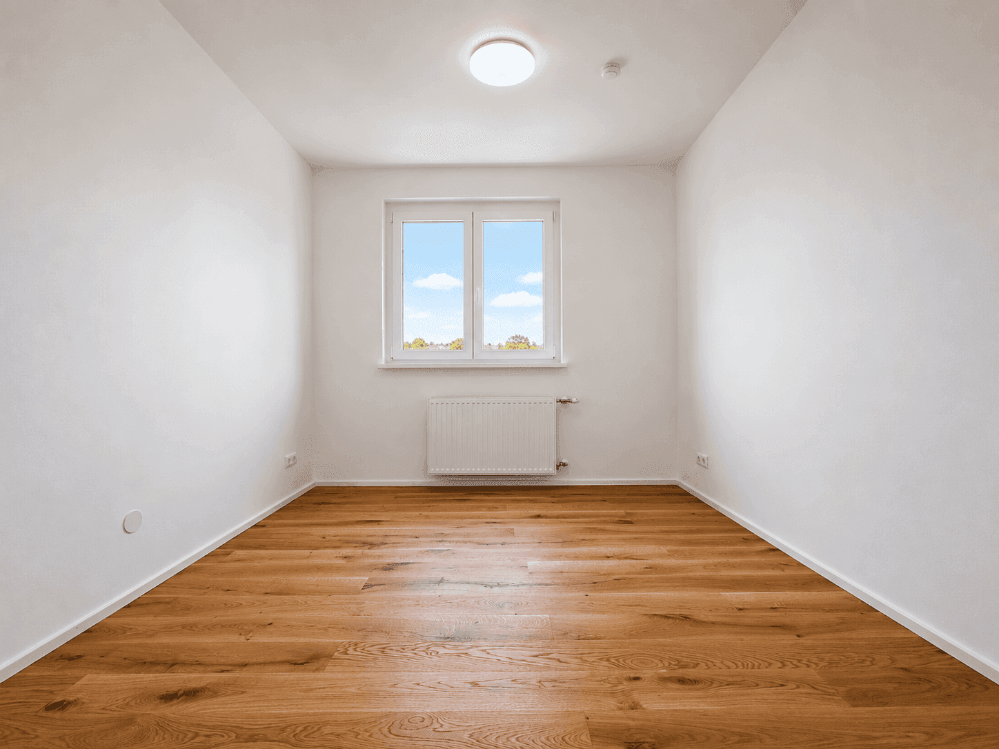 Helles Zimmer mit Holzboden und einem Fenster, das einen Blick nach draußen bietet.