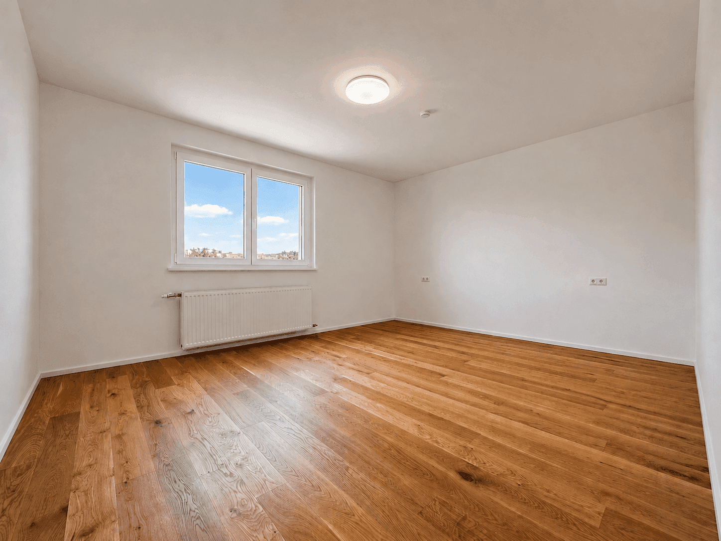 Geräumiges Schlafzimmer mit Holzboden und großem Fenster, das viel Tageslicht hereinlässt.