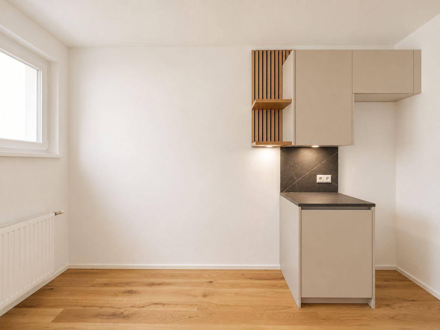 Heller Küchenbereich mit Holzboden und modernen Schränken, bereit für die Installation weiterer Geräte.