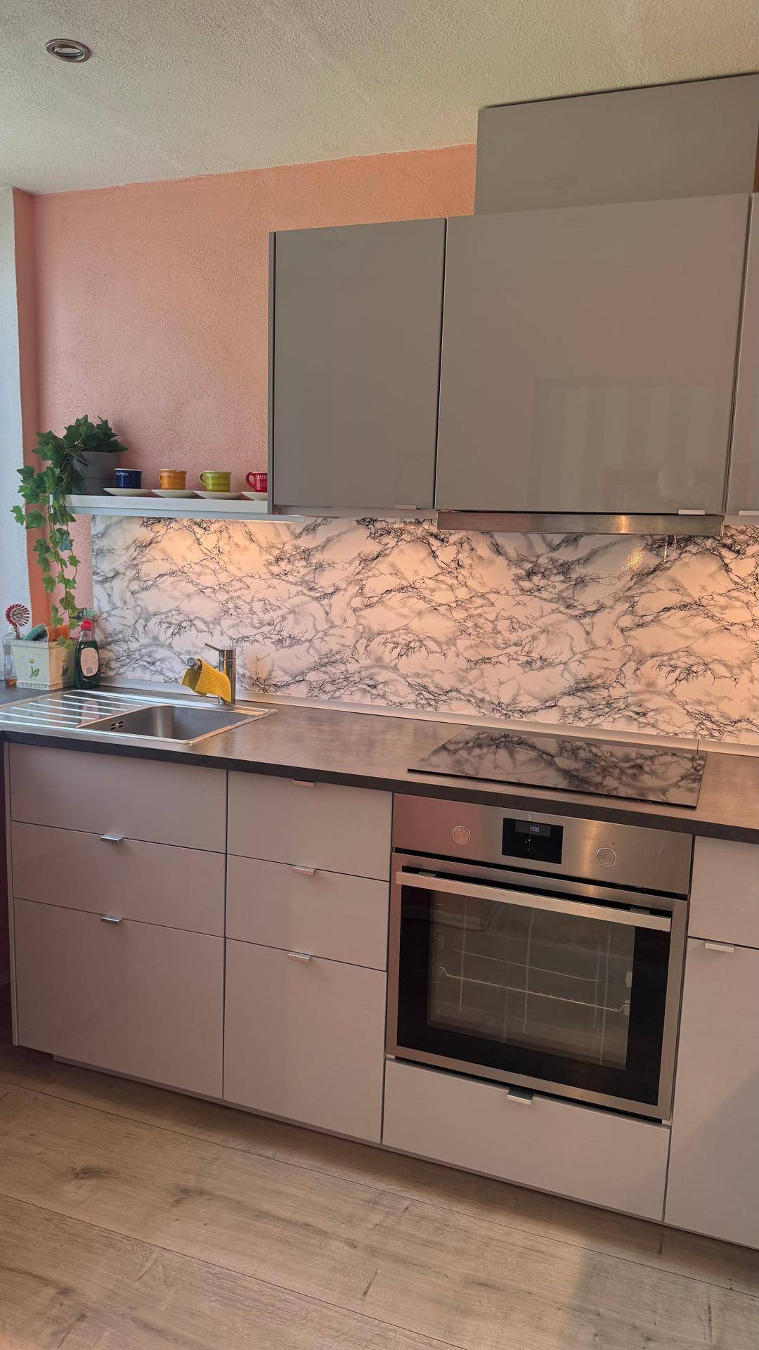 Moderne Küche mit grauen Schränken, Marmoroptik-Rückwand und integrierten Geräten.