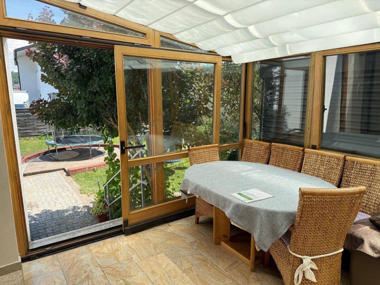 Heller Wintergarten mit Zugang zum Garten, Blick auf die Grünfläche und ein Trampolin.