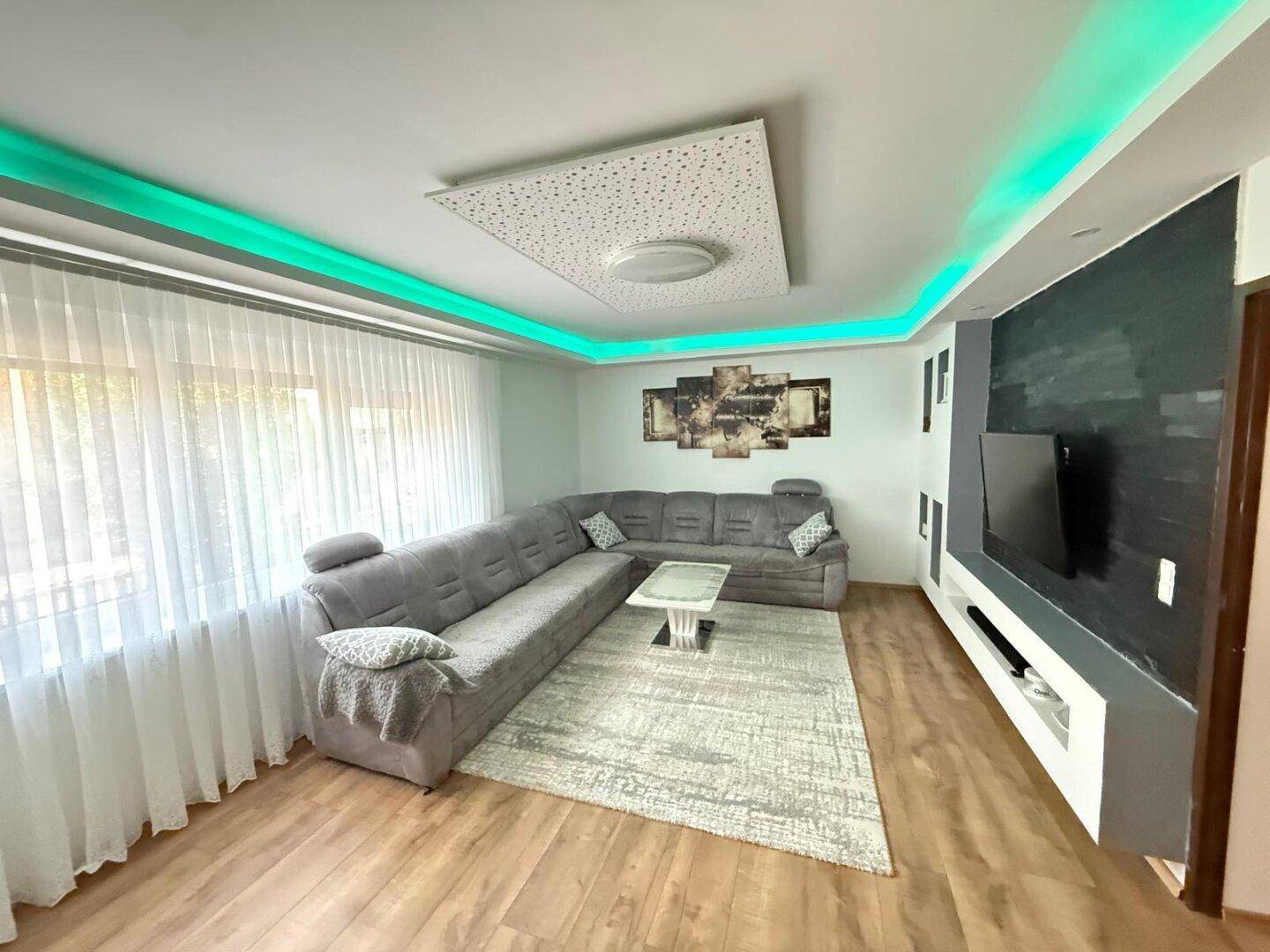Modernes Wohnzimmer mit großem Ecksofa, TV-Wand und dekorativer Deckenbeleuchtung.
