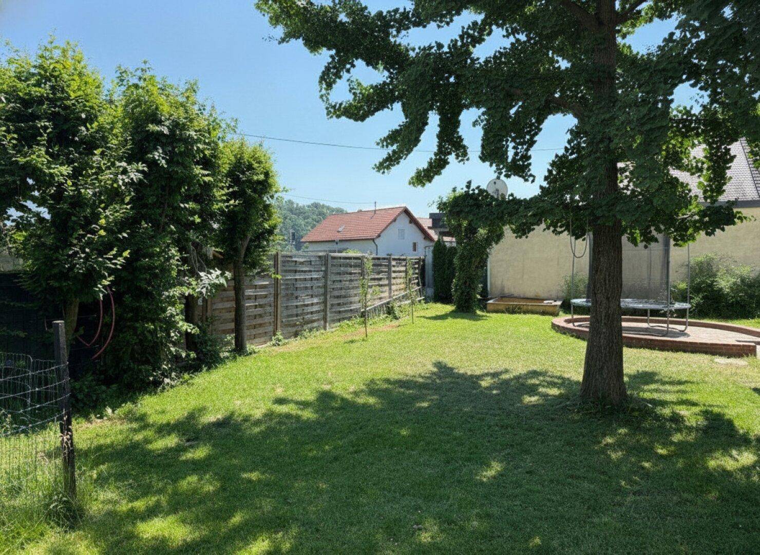 Großer, gepflegter Garten mit Rasenfläche, Bäumen und einem Trampolin im Hintergrund.