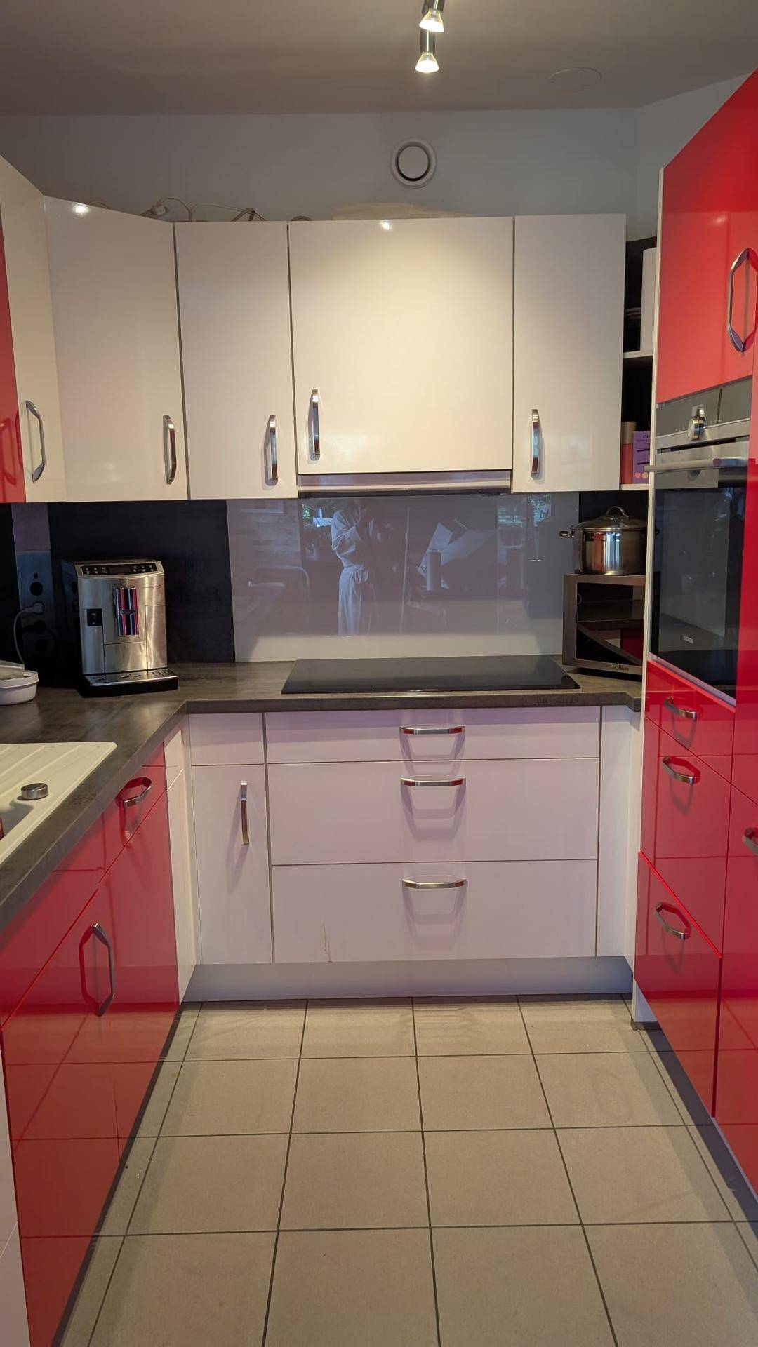 Funktionale Küche mit roten und weißen Schränken, Induktionskochfeld und Fliesenboden.
