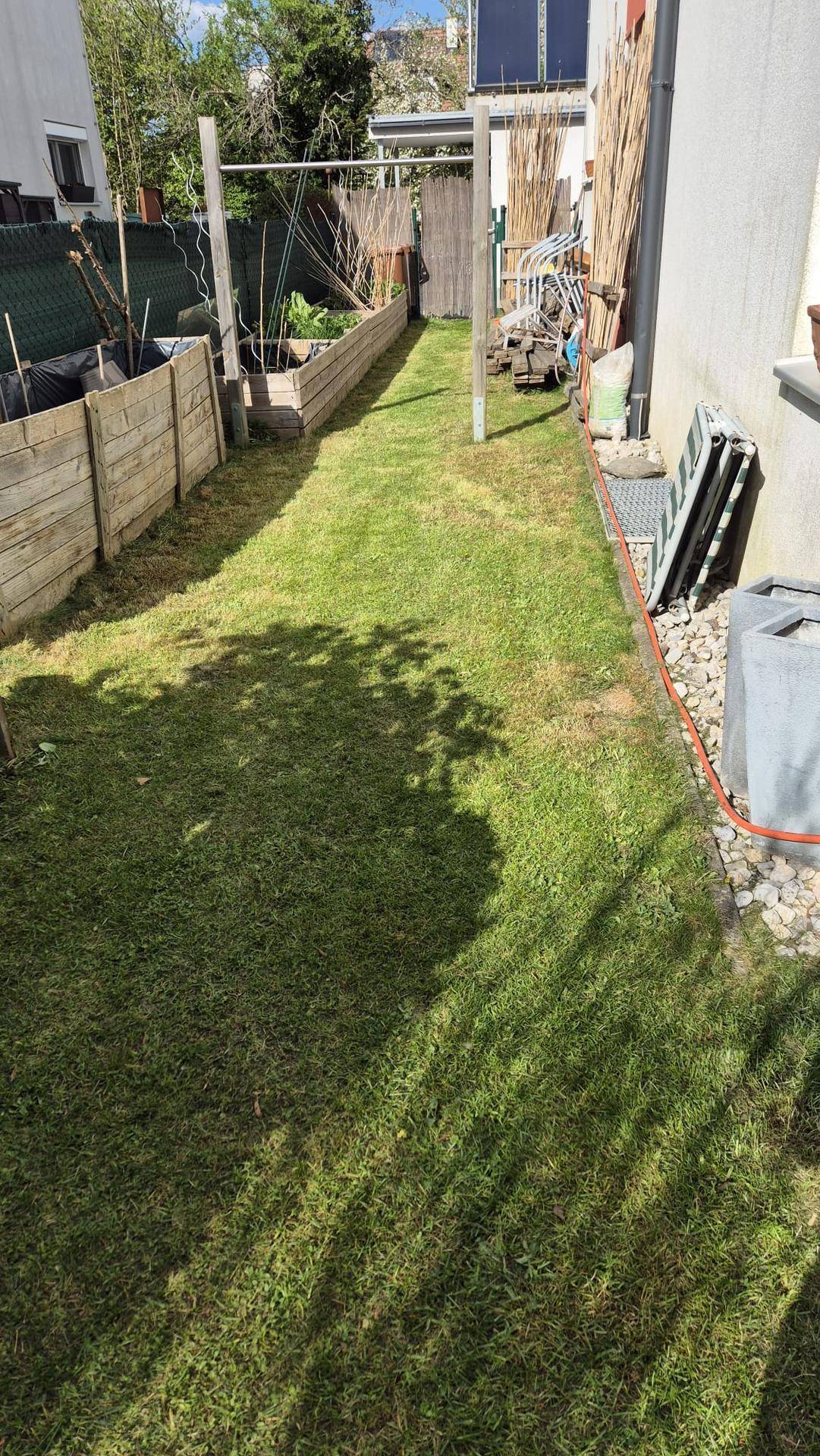 Langer, schmaler Gartenbereich mit Rasen, Hochbeeten und seitlichem Zugang zum Haus.