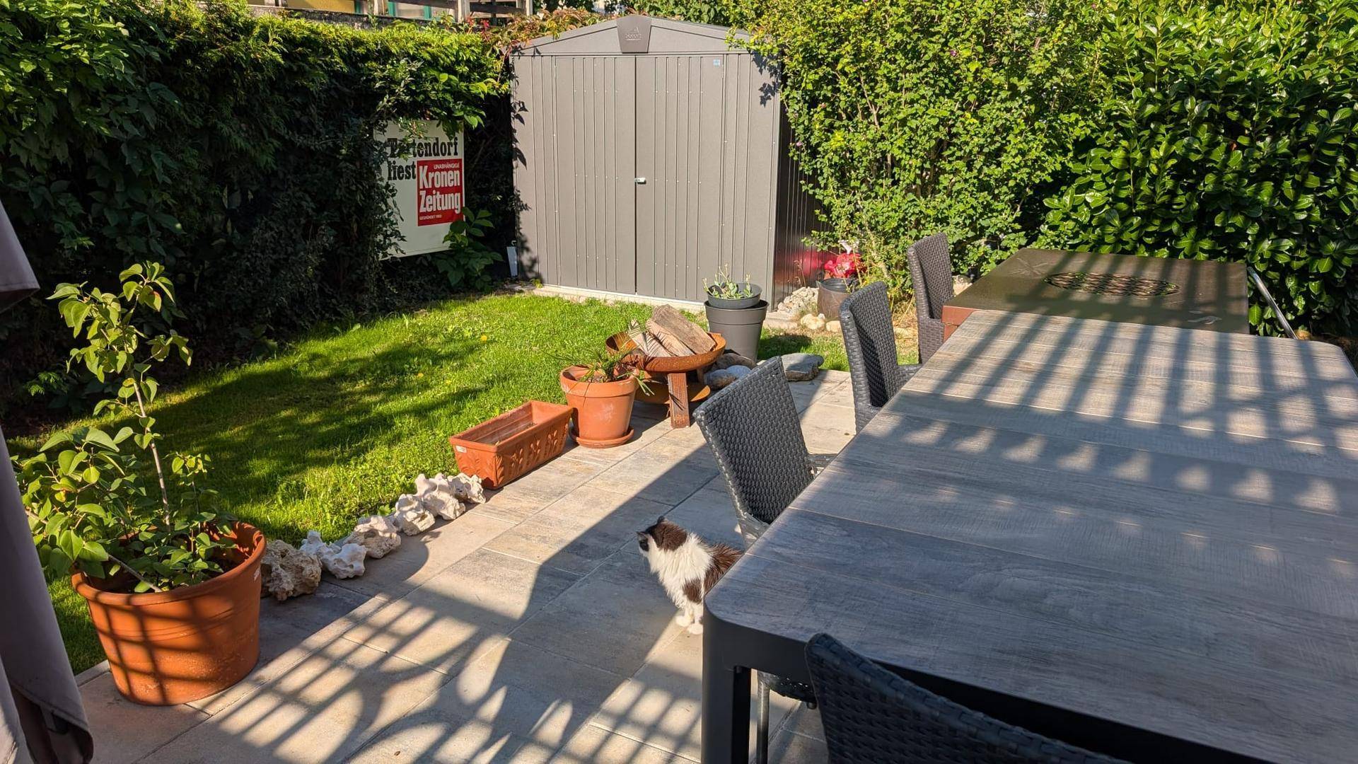 Gemütliche Terrasse mit großem Esstisch und Blick auf den Garten mit praktischem Geräteschuppen.