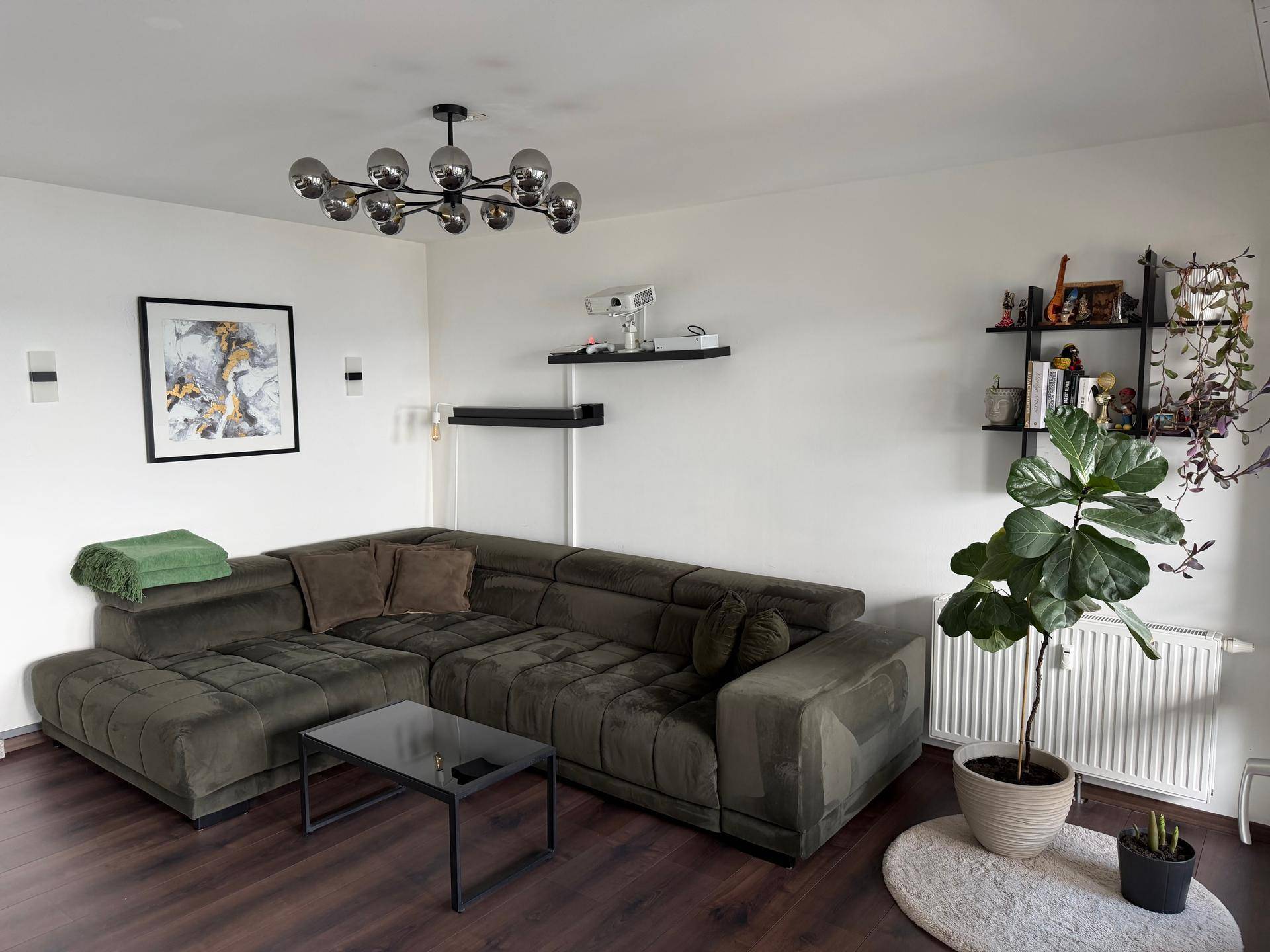 Gemütliches Wohnzimmer mit großem Ecksofa, Wandregalen und Zimmerpflanze.