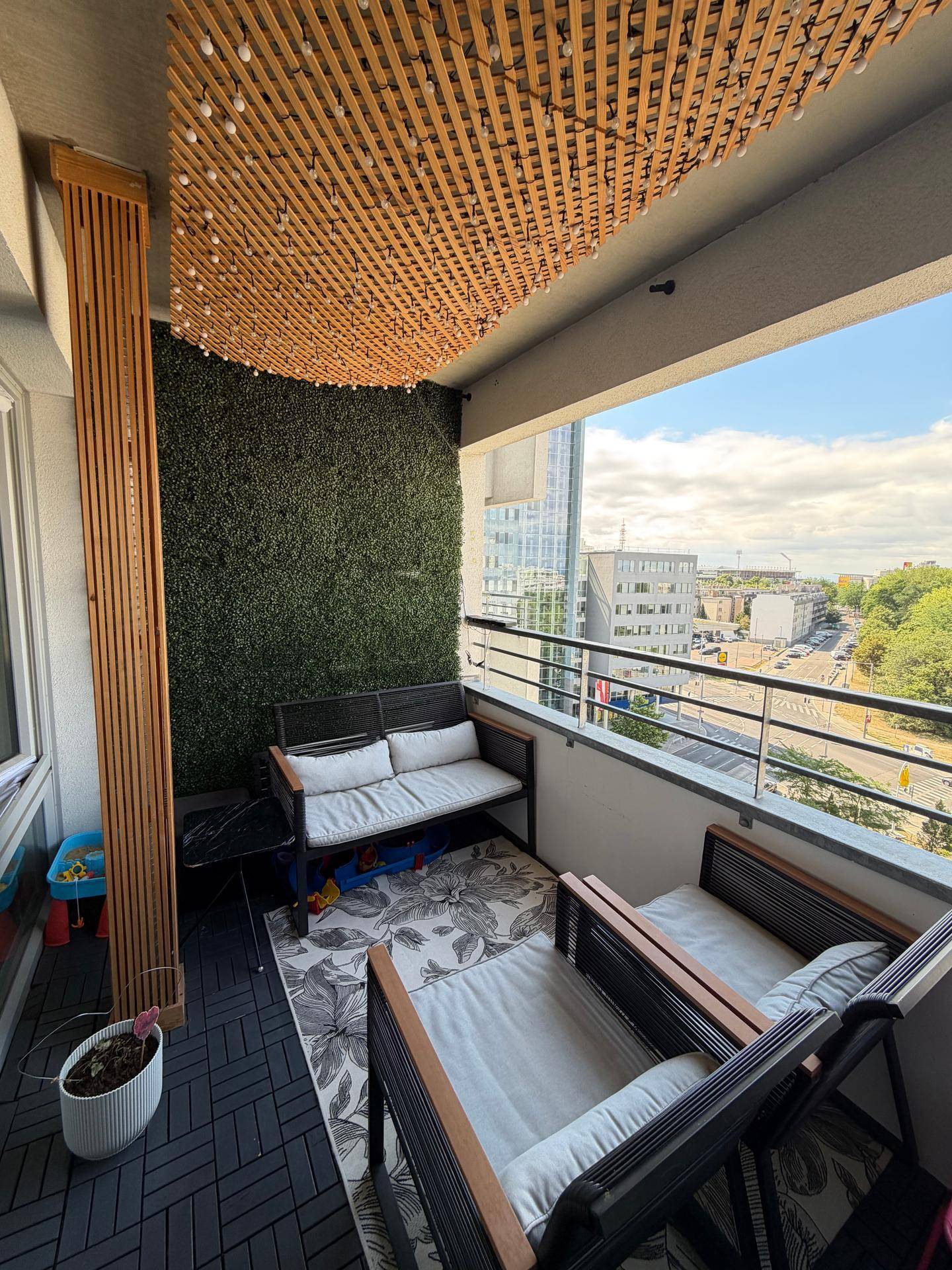 Gemütlicher Balkon mit Sitzgelegenheiten, grüner Wand und Blick auf die Stadt.