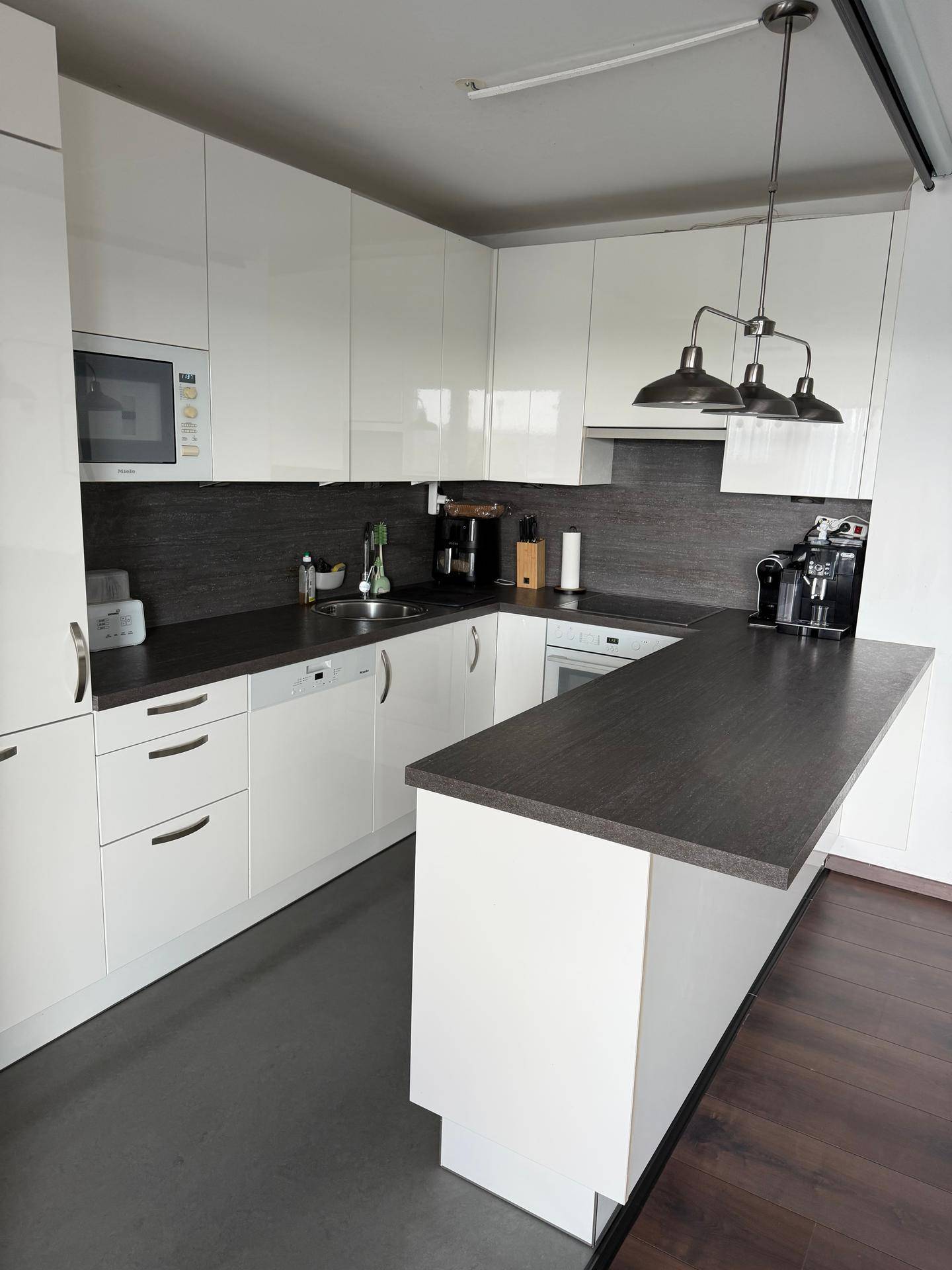 Moderne weiße Küche mit dunkler Arbeitsplatte, integrierten Geräten und Kochinsel.