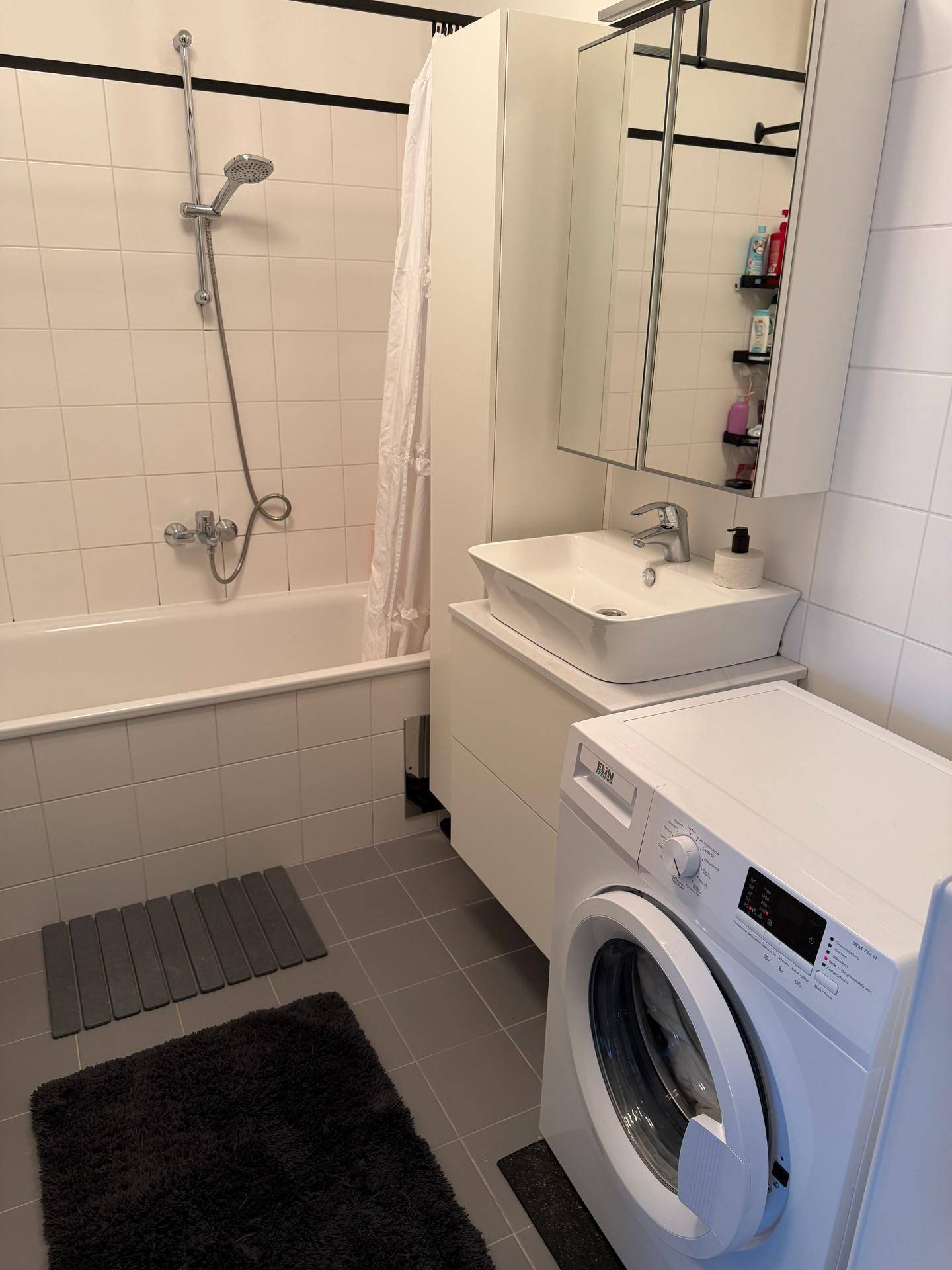 Funktionales Badezimmer mit Badewanne, Waschbecken und integrierter Waschmaschine.