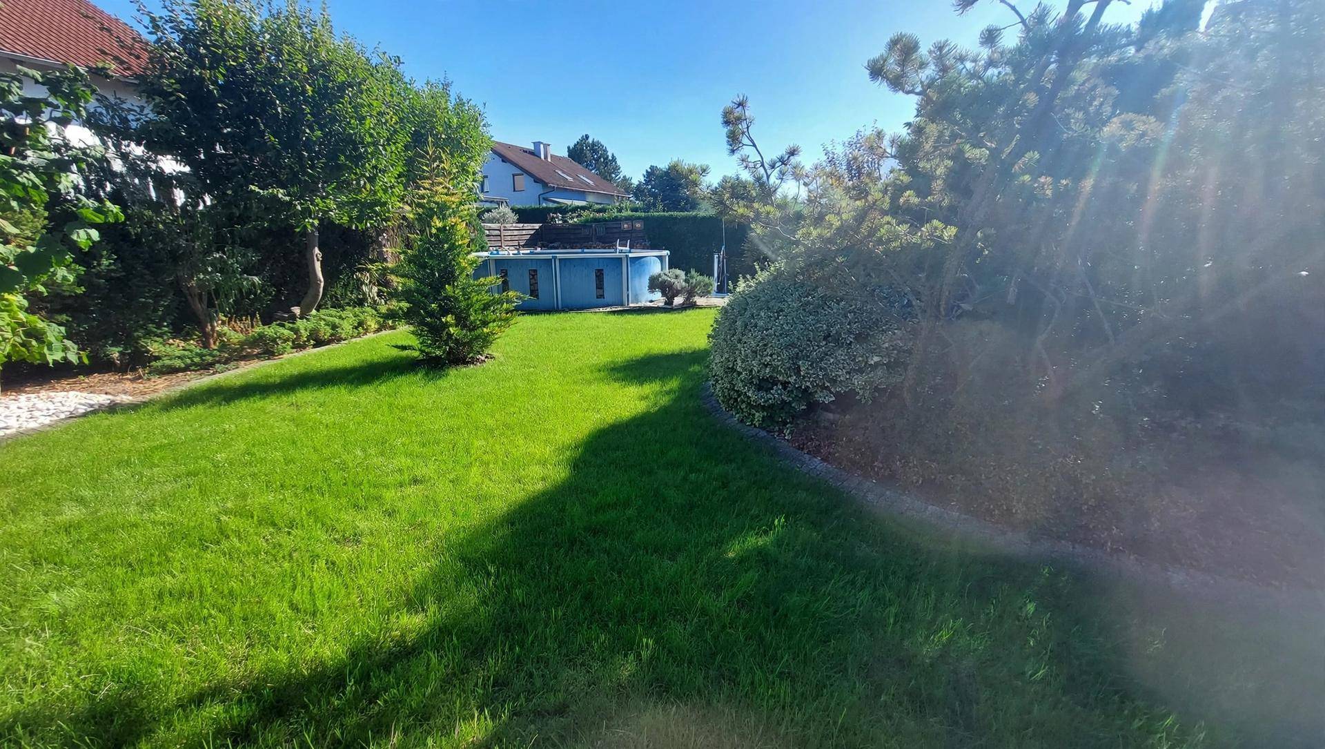 Großer Garten mit Rasenfläche, Bäumen und einem kleinen Aufstellpool im Hintergrund.