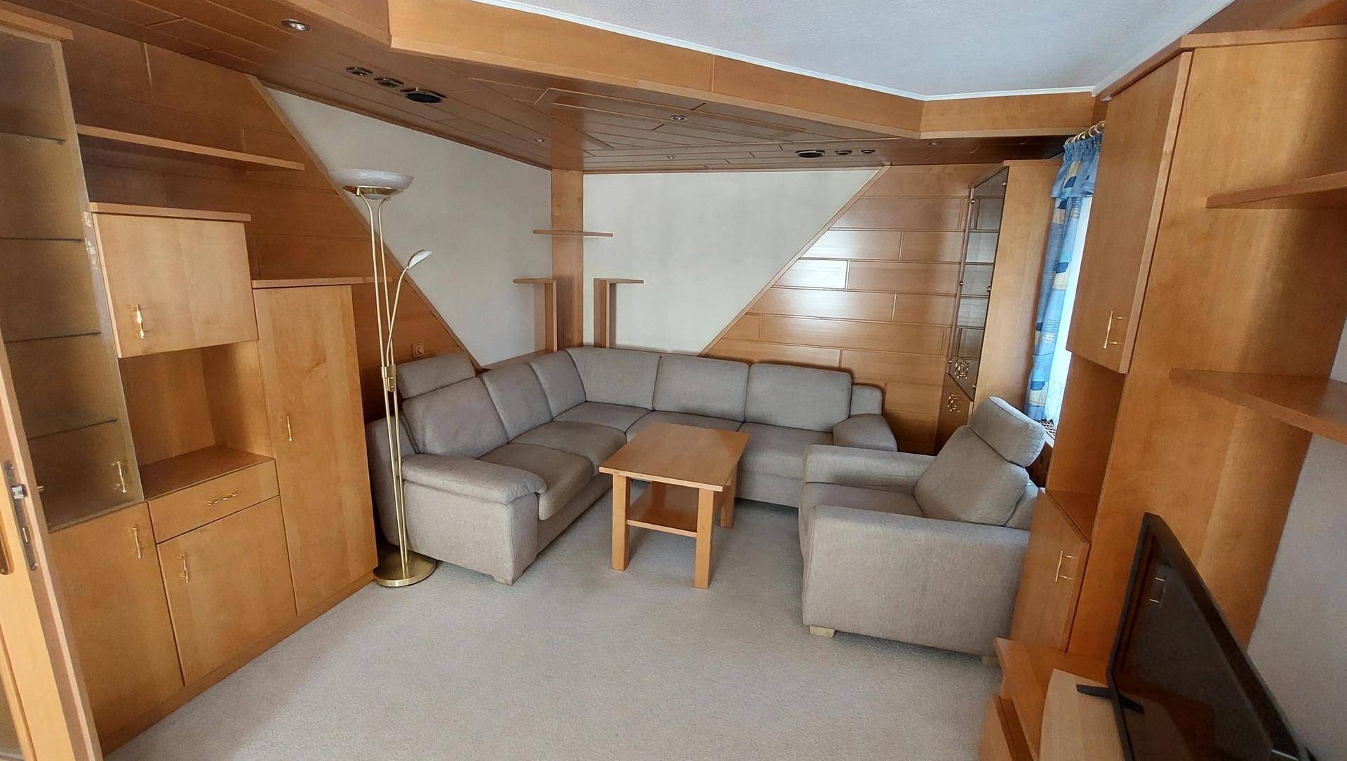 Wohnzimmer mit Holzverkleidung, Ecksofa und Teppichboden, bietet eine gemütliche Atmosphäre.