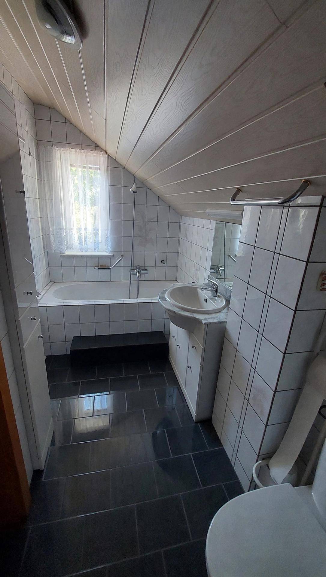 Badezimmer im Dachgeschoss mit Badewanne, Waschtisch und dunklen Bodenfliesen.