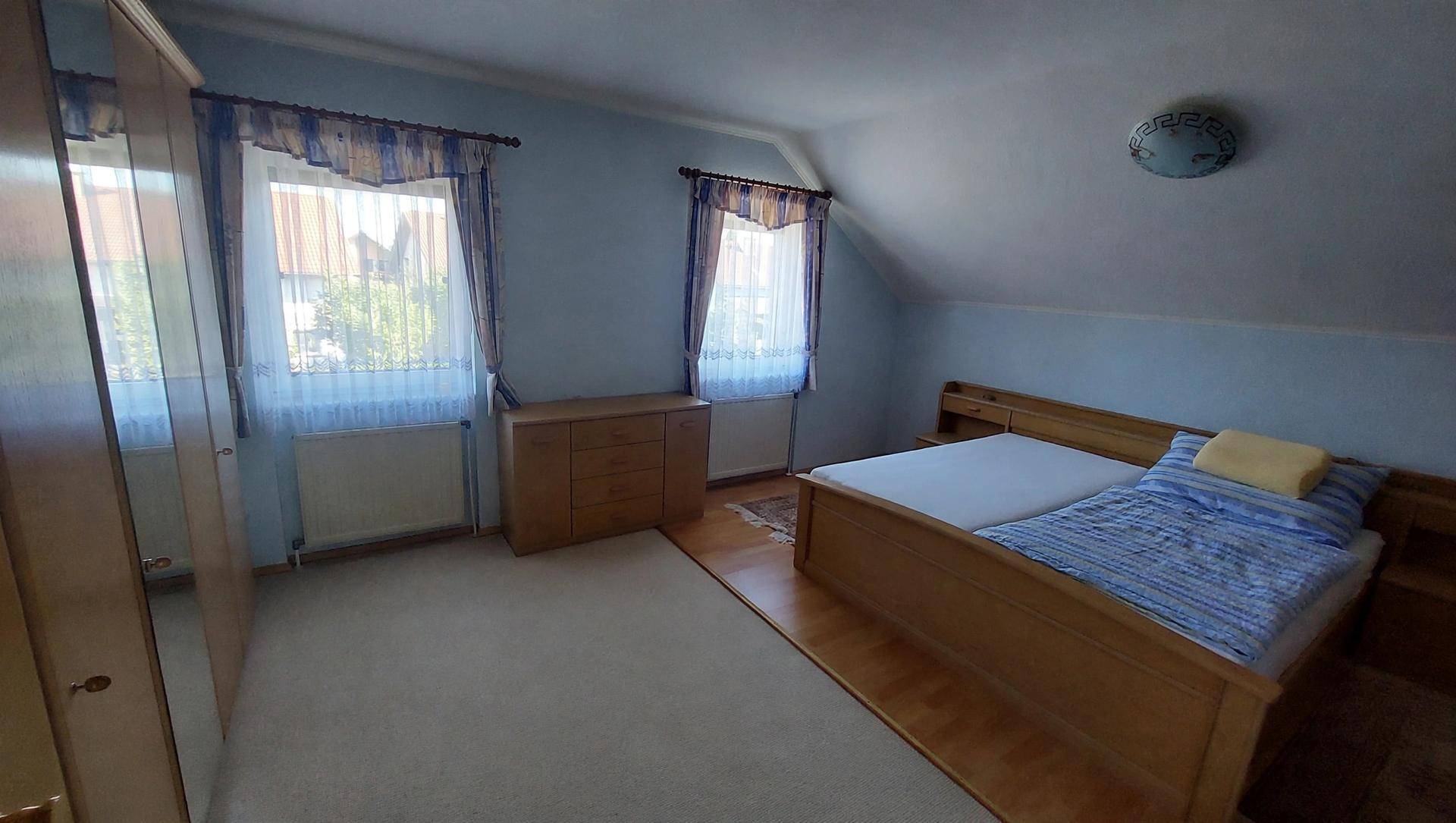 Helles Schlafzimmer im Dachgeschoss mit Doppelbett, Teppichboden und zwei Fenstern.
