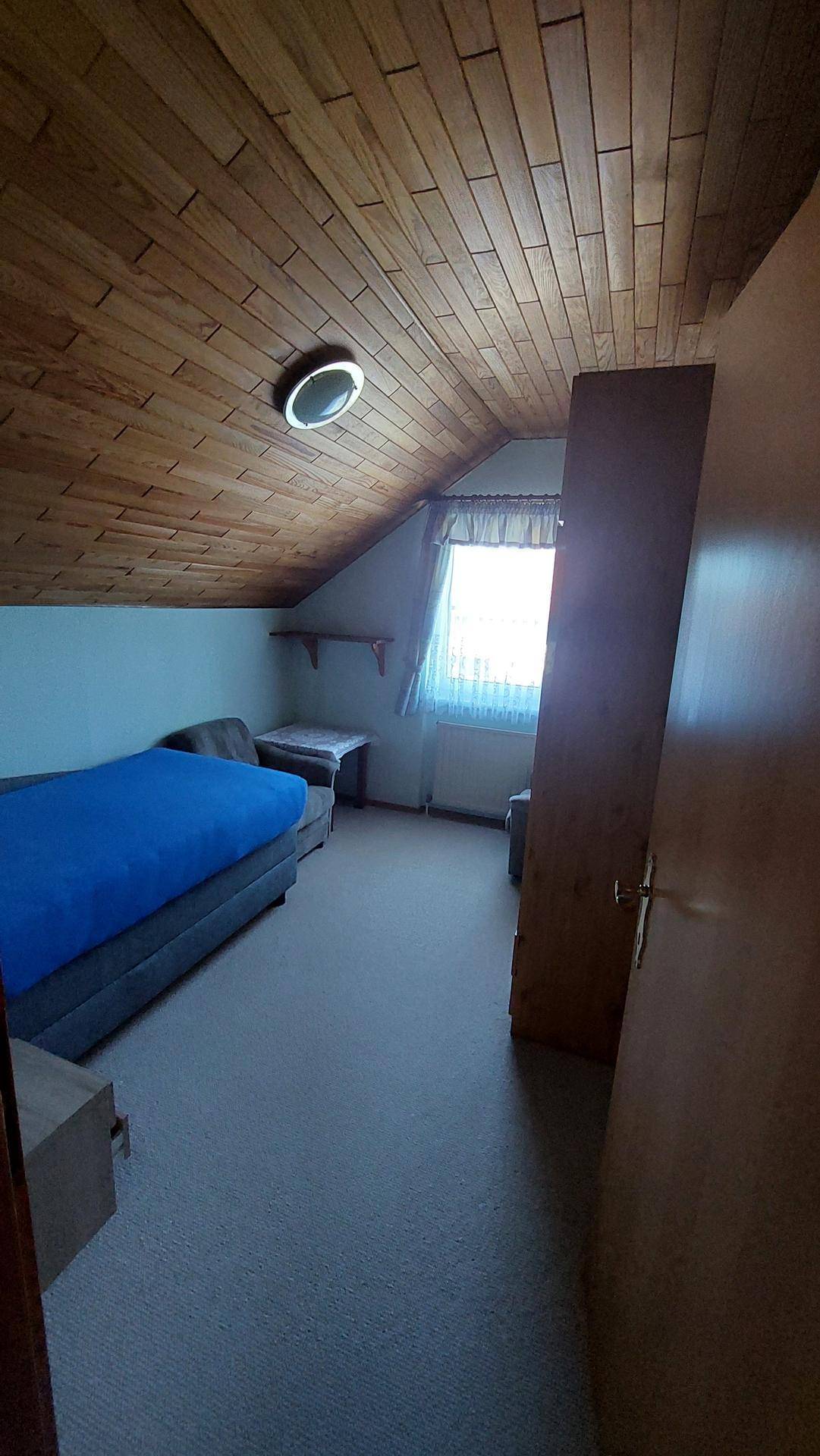 Schlafzimmer im Dachgeschoss mit Holzdecke, Teppichboden und Einzelbett.