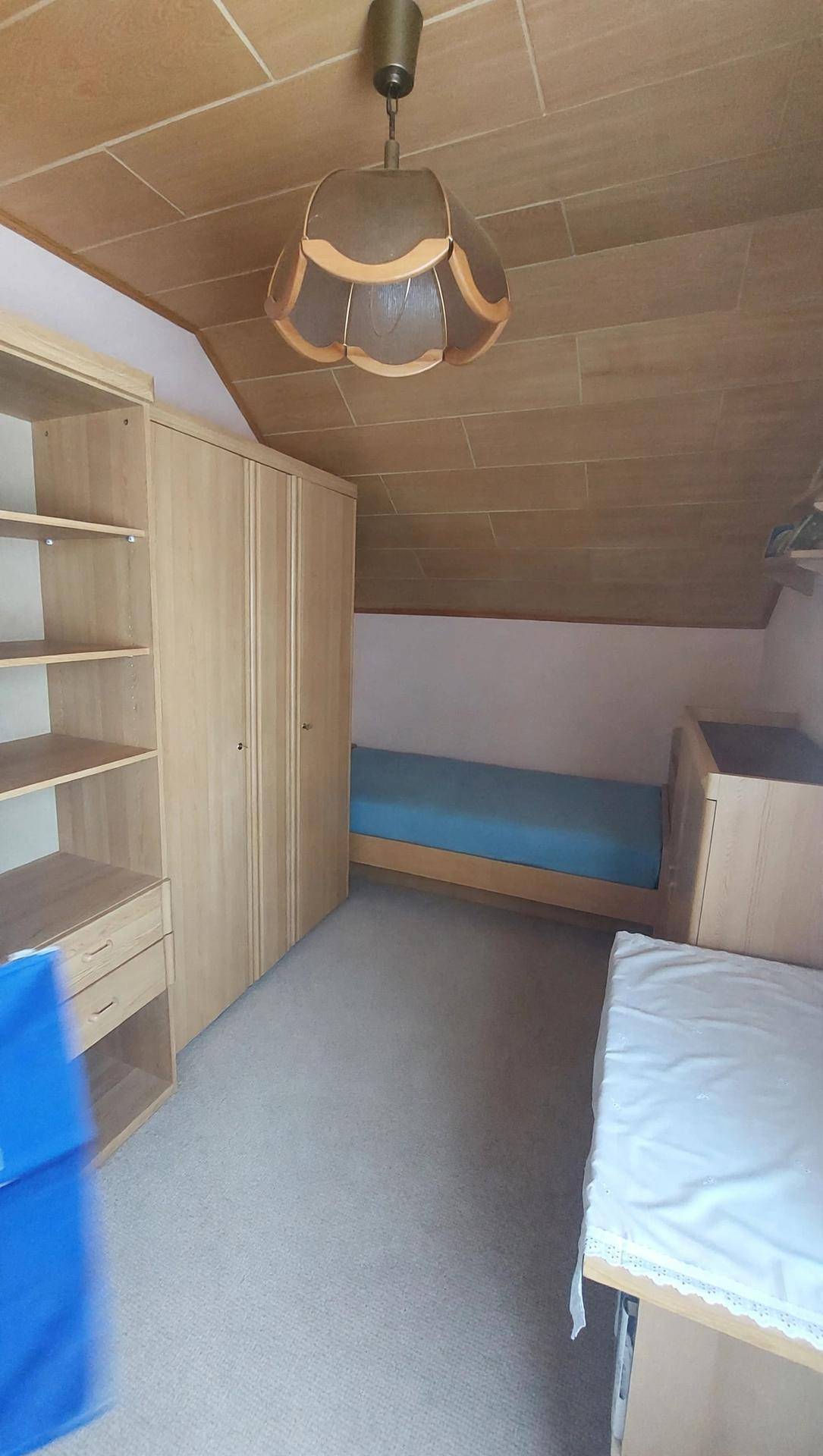 Schlafzimmer im Dachgeschoss mit Holzdecke, Teppichboden und Einzelbett.