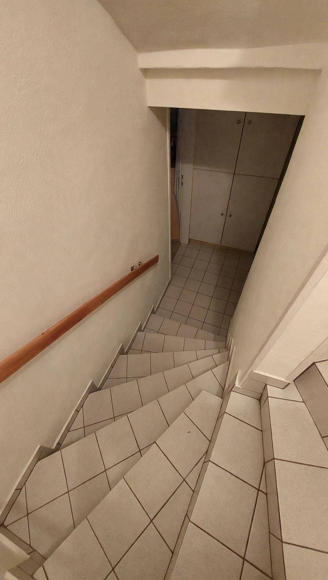 Treppenhaus mit gefliesten Stufen und Holzgeländer führt ins Untergeschoss.