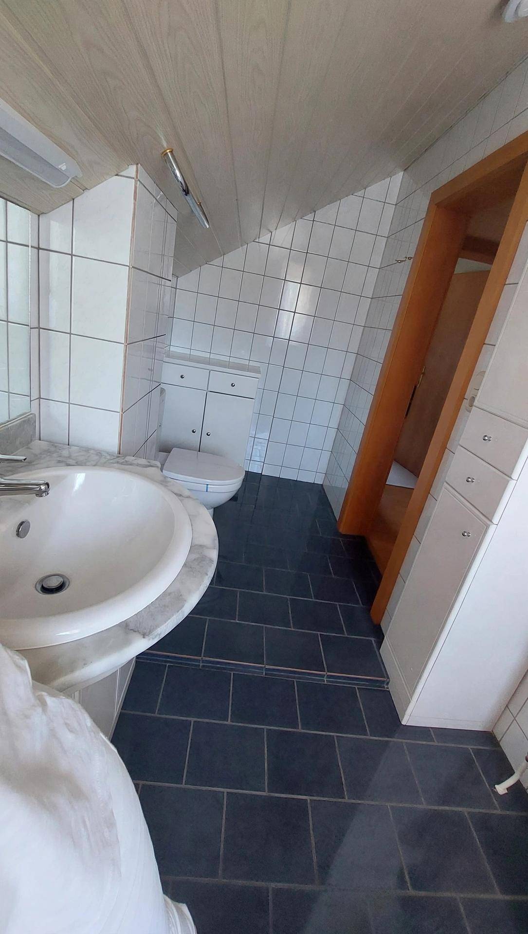 Badezimmer im Dachgeschoss mit Waschtisch, Toilette und dunklen Bodenfliesen.