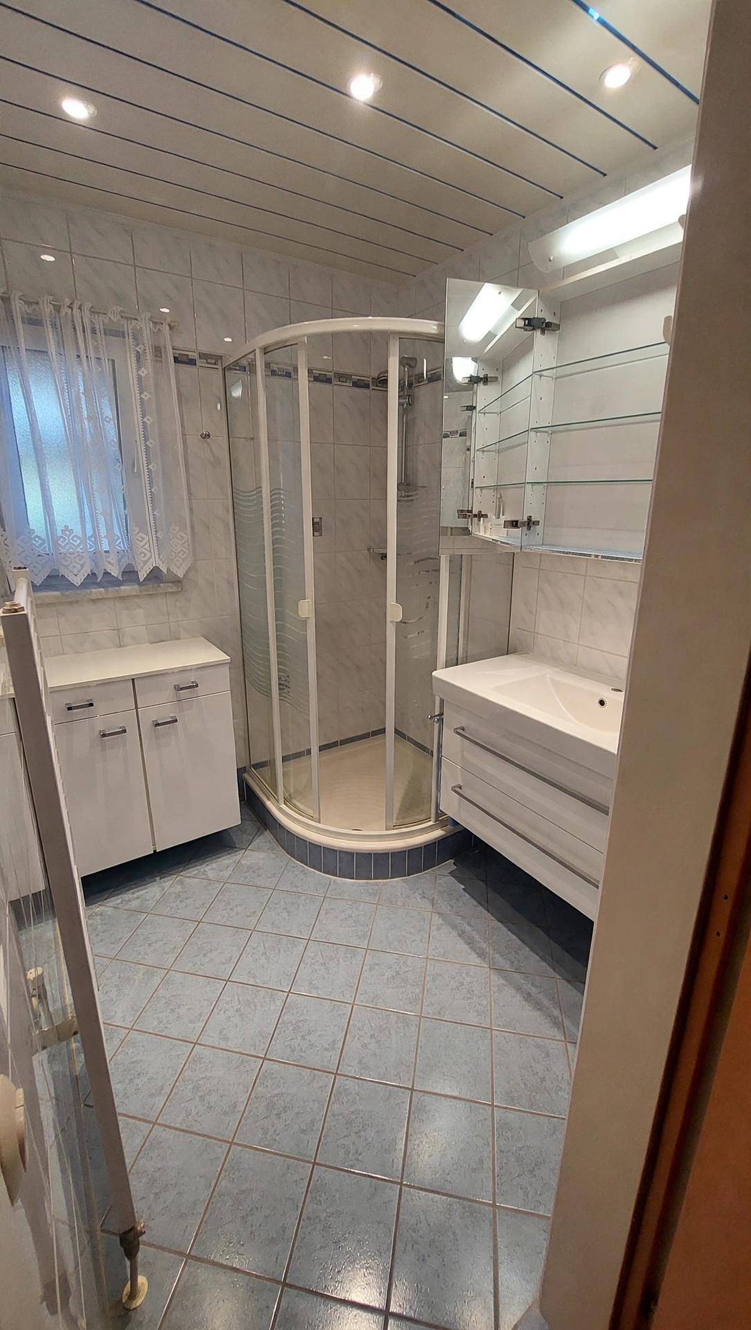 Badezimmer mit blauen Fliesen, Duschkabine und modernem Waschtisch.