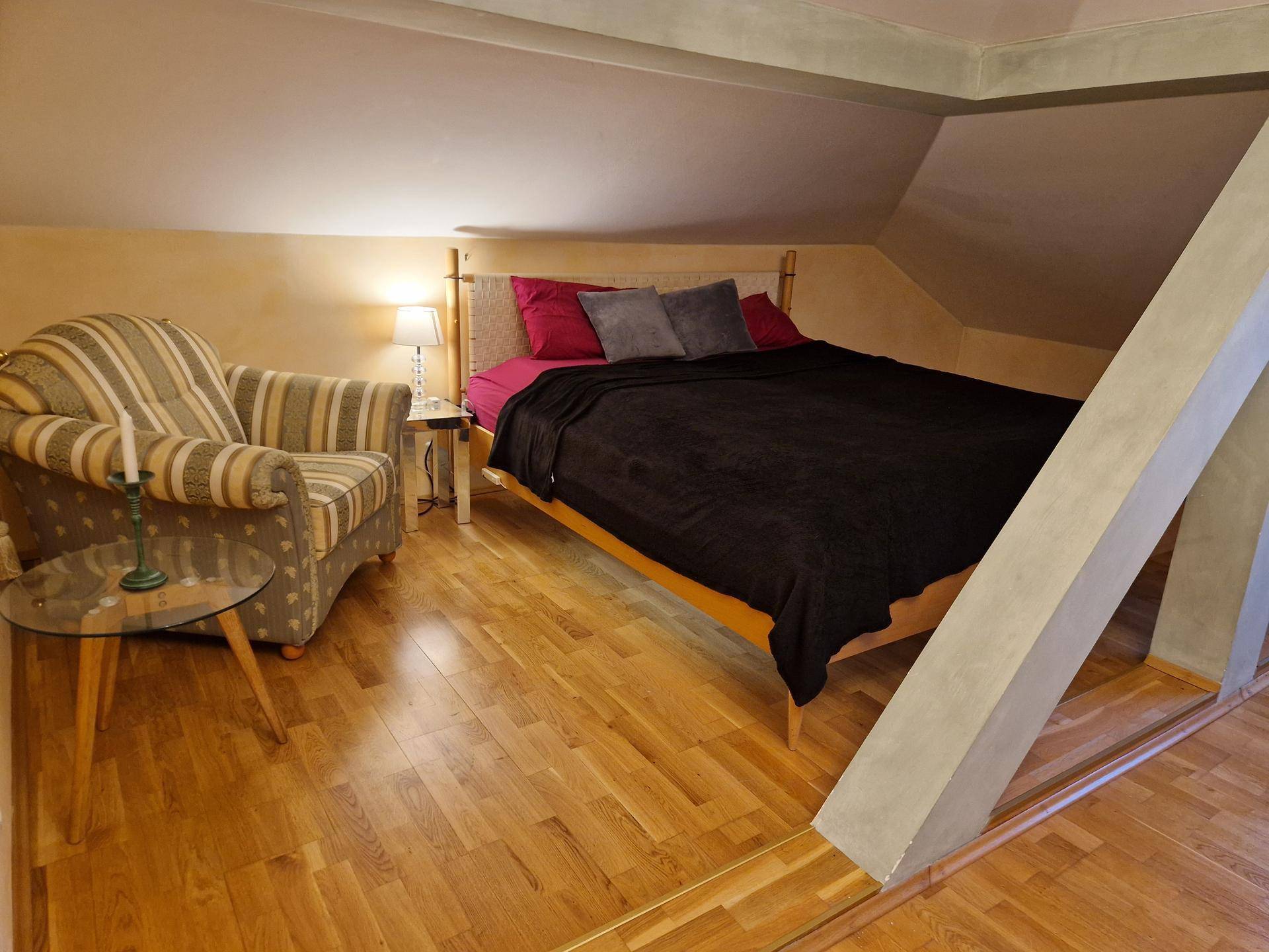 Gemütliches Schlafzimmer im Dachgeschoss mit Holzboden, schrägen Wänden und bequemen Sessel.