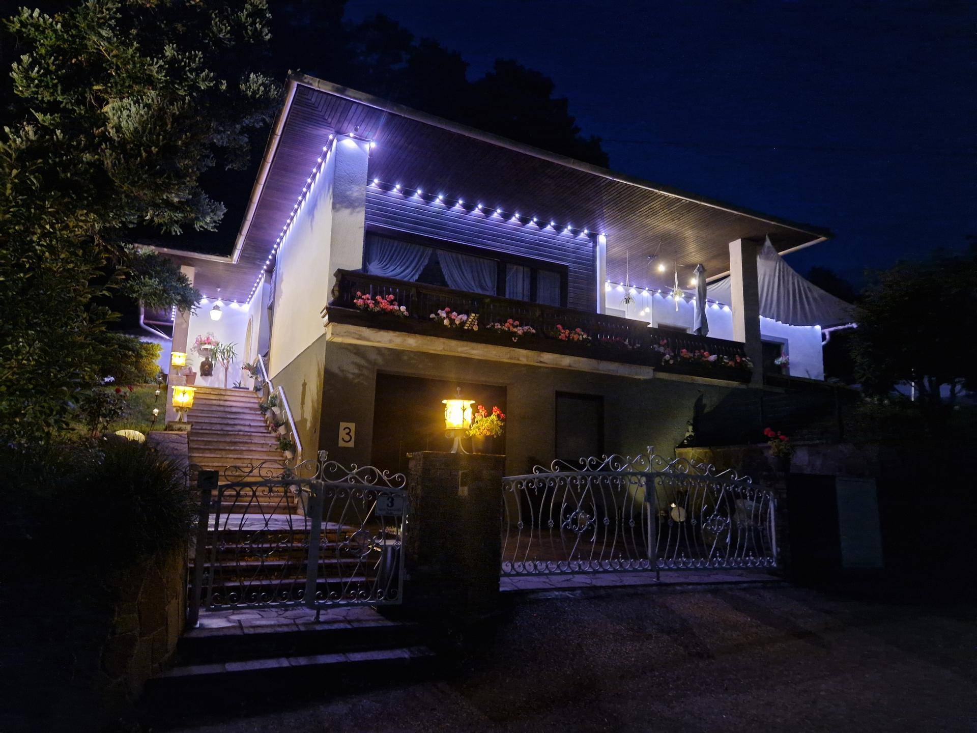 Ansicht des Hauses bei Nacht mit dekorativer Beleuchtung und Zugang zum Balkon.