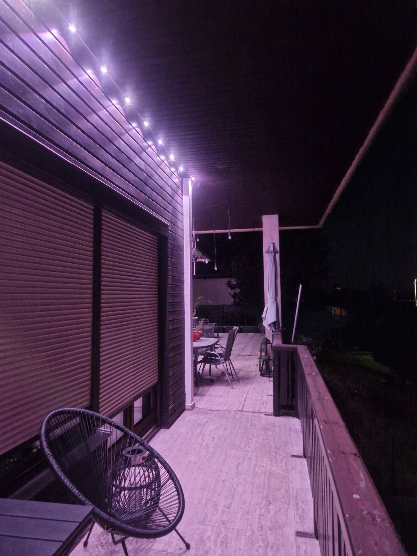 Beleuchteter Balkon bei Nacht mit gemütlicher Sitzgelegenheit und Rollläden.