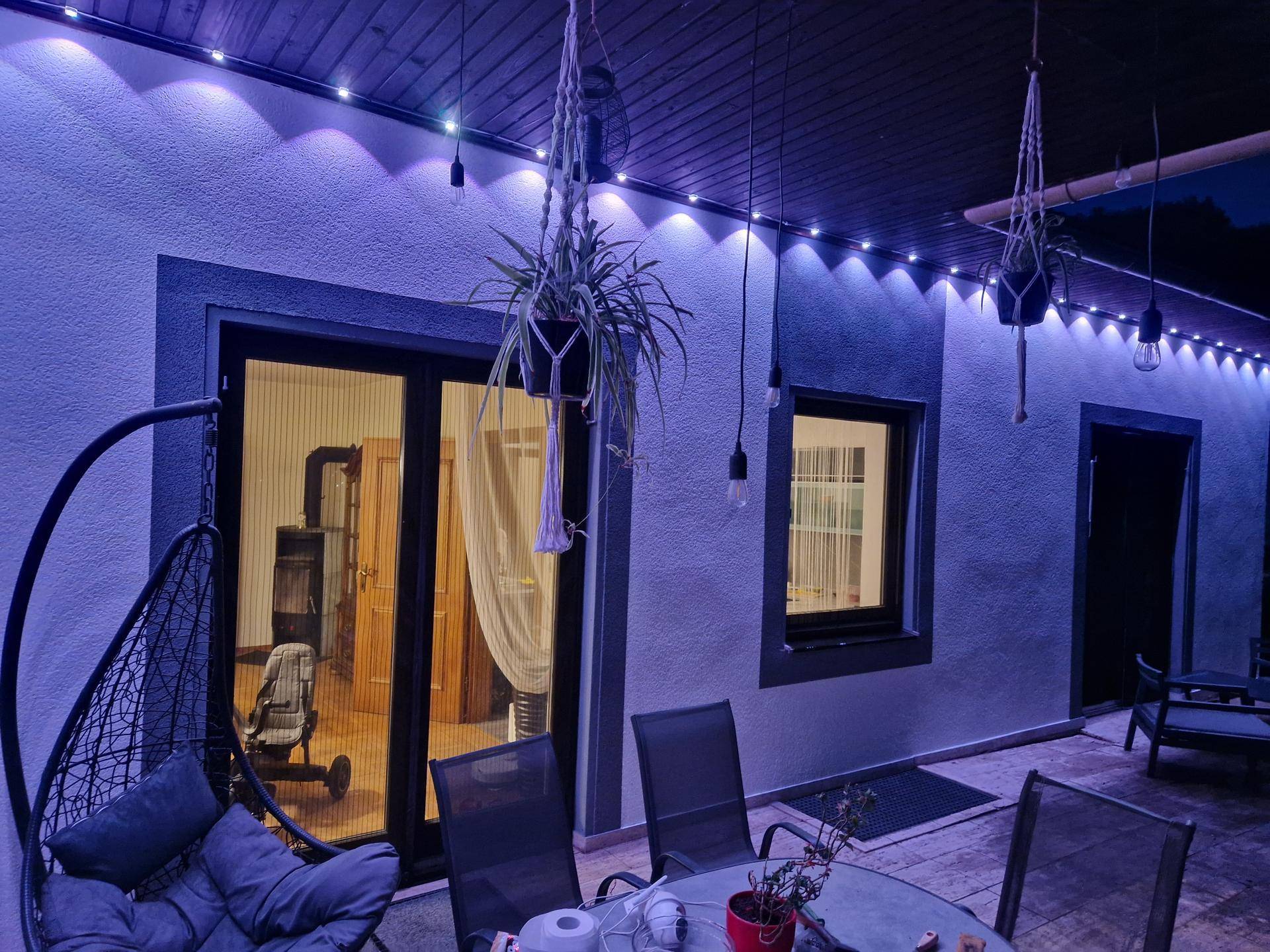 Gemütliche Terrasse bei Nacht mit Sitzmöbeln und Blick in den beleuchteten Innenraum.