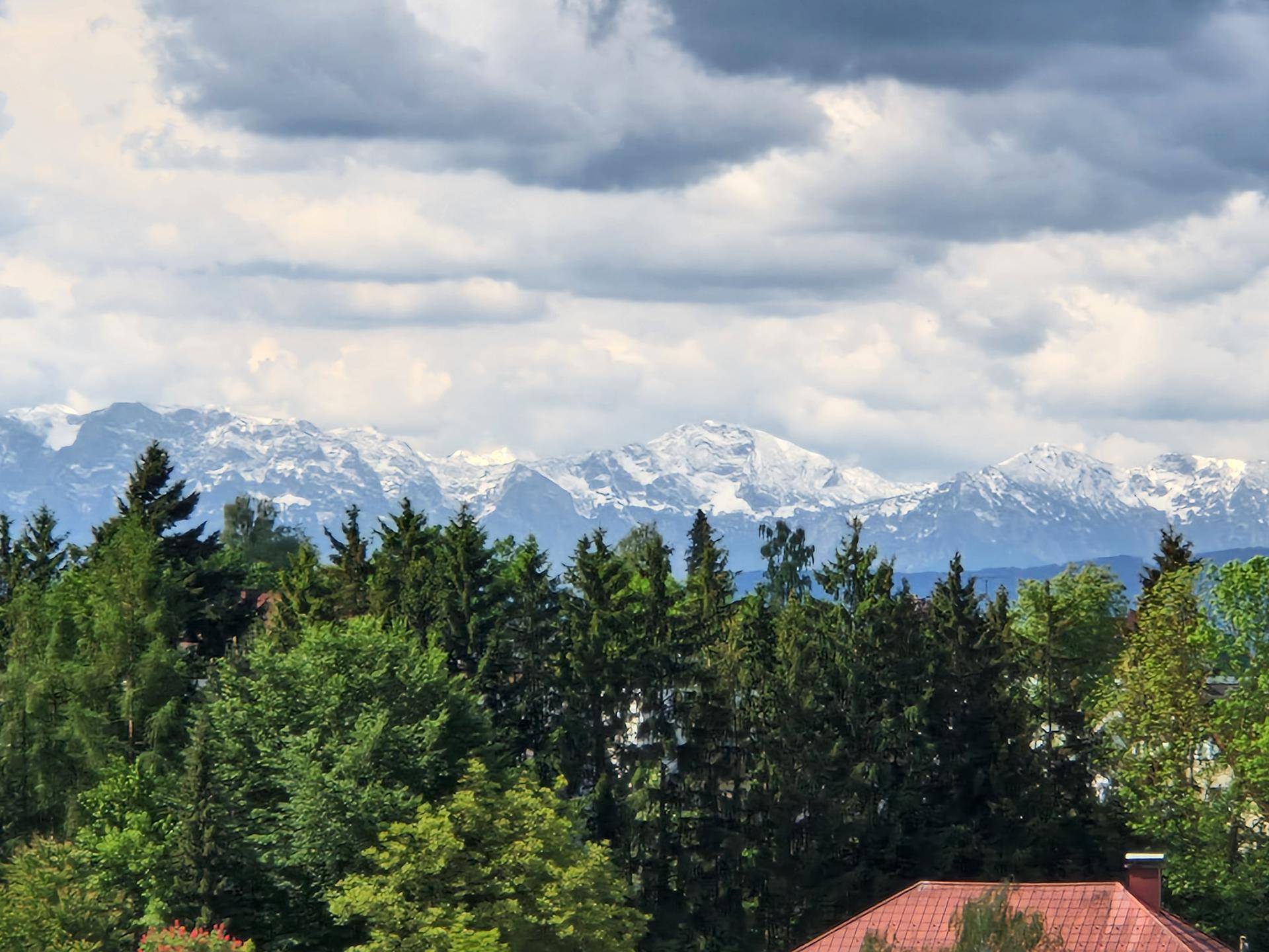 Malerischer Bergblick mit schneebedeckten Gipfeln über grünen Baumwipfeln.