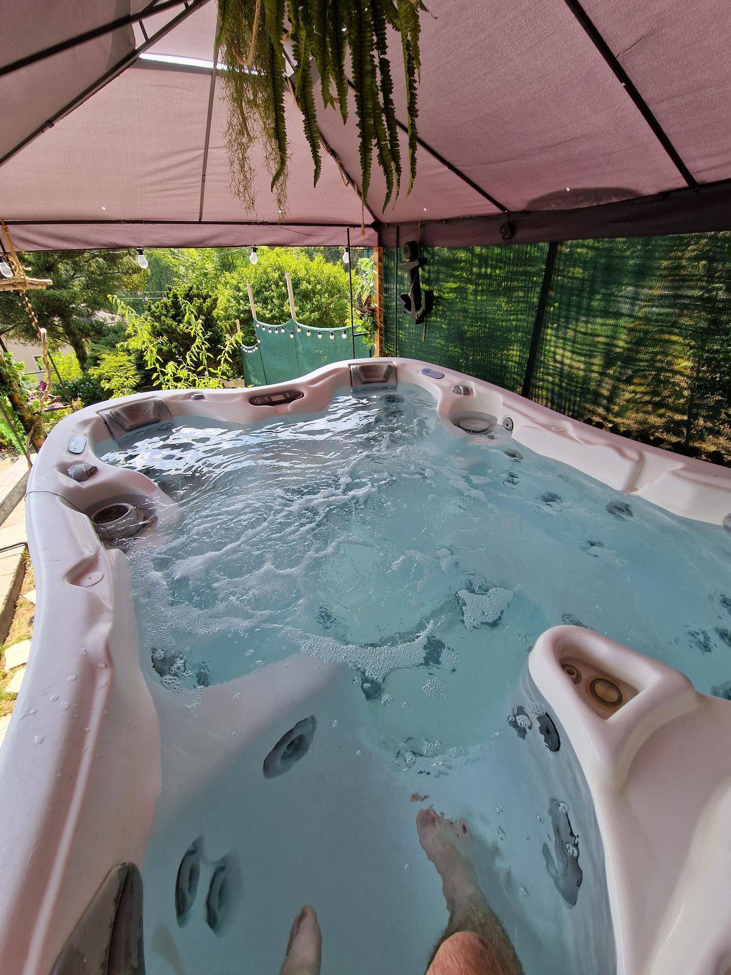 Entspannender Whirlpool im Freien unter einem schützenden Pavillon, umgeben von Grün.