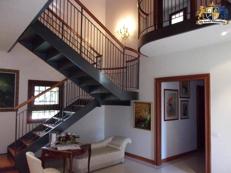 Heller Eingangsbereich mit eleganter geschwungener Treppe und hohen Decken, die zum Obergeschoss führt.