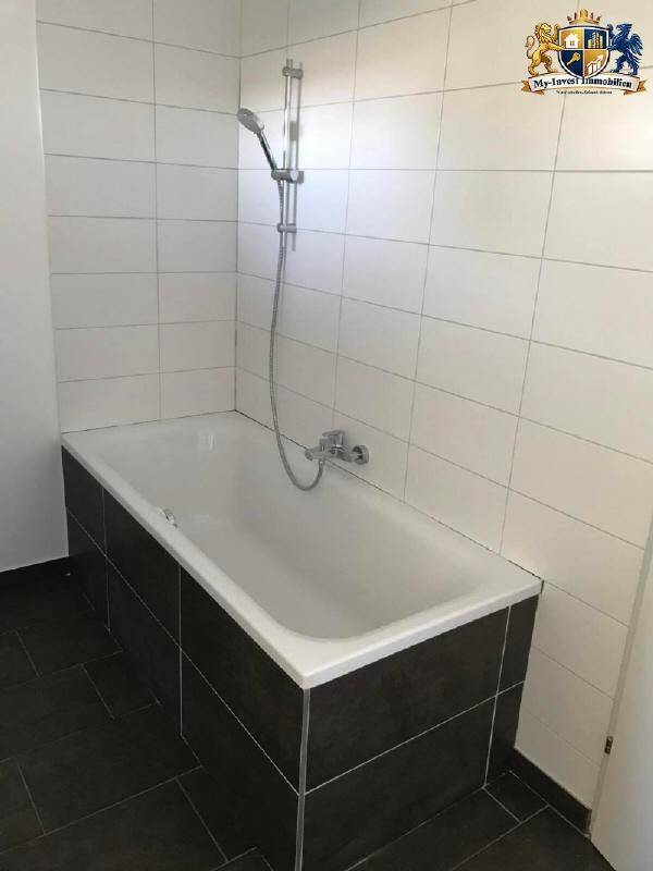 Modernes Badezimmer mit Badewanne und Duscharmatur, weißen Wandfliesen und dunklem Boden.