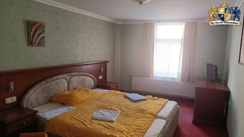 Schlafzimmer mit Doppelbett, Holzmöbeln und gemusterter Tapete.