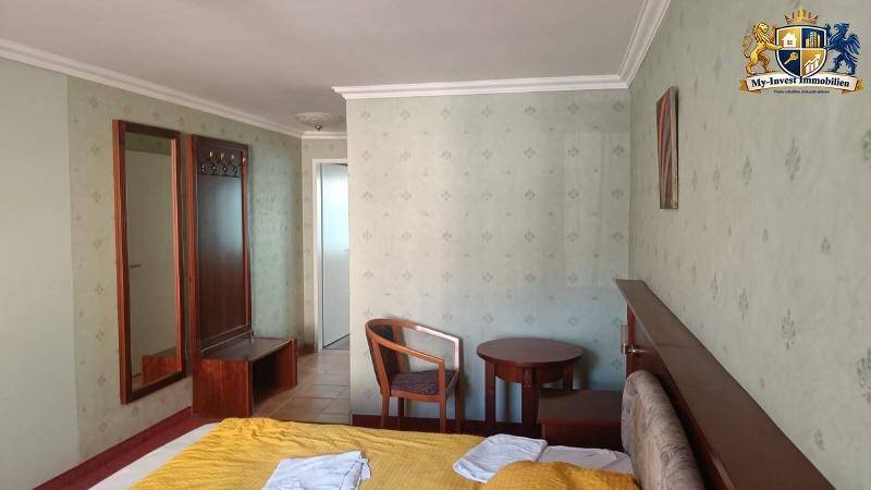Helles Schlafzimmer mit Einzelbett, Holzmöbeln und gemusterter Tapete.