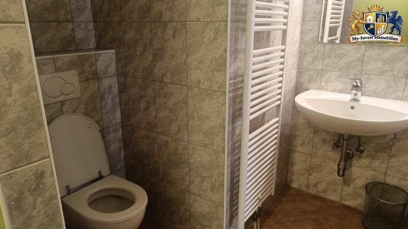 Kleines Badezimmer mit Fliesen, WC, Waschbecken und beheiztem Handtuchhalter.