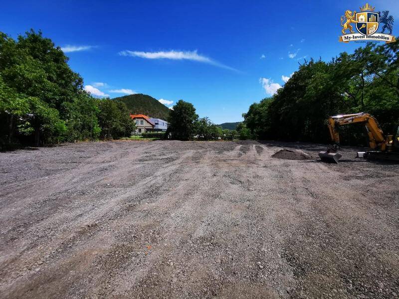 Weitläufiges Baugrundstück mit Blick auf umliegende Häuser und grüne Hügel unter blauem Himmel.