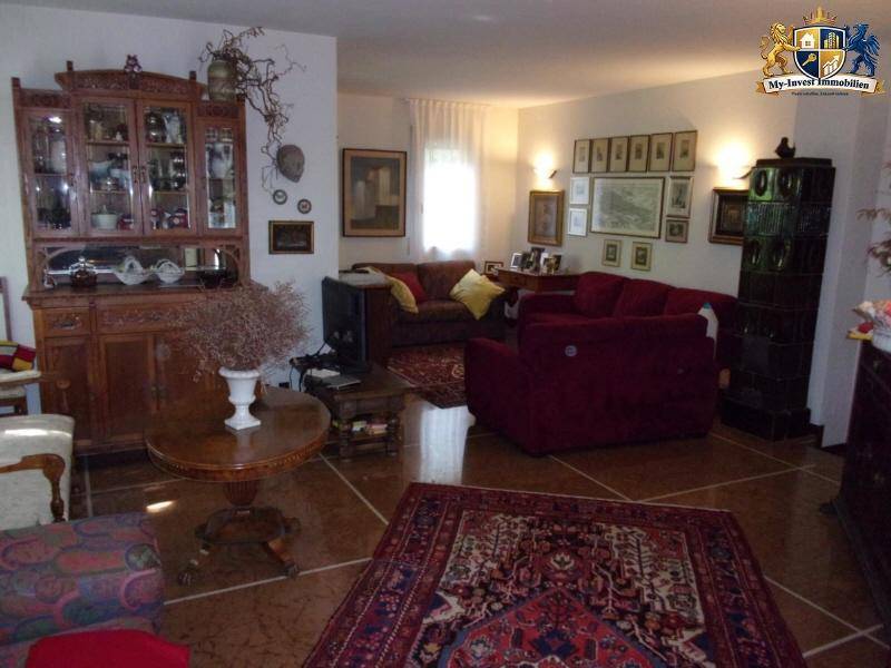 Geräumiges Wohnzimmer mit traditionellen Holzmöbeln, Teppichen und einem dekorativen Kachelofen.