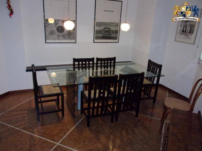 Esszimmer mit modernem Glastisch und dunklen Holzstühlen, beleuchtet von stilvollen Hängelampen.
