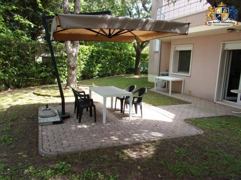 Gemütliche gepflasterte Terrasse mit Esstisch, Stühlen und großem Sonnenschirm im Garten.