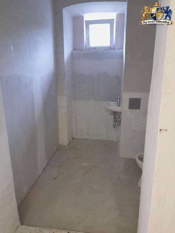 Unfertiges Badezimmer mit Fenster, Toilette und Waschbecken, wartet auf Fertigstellung.