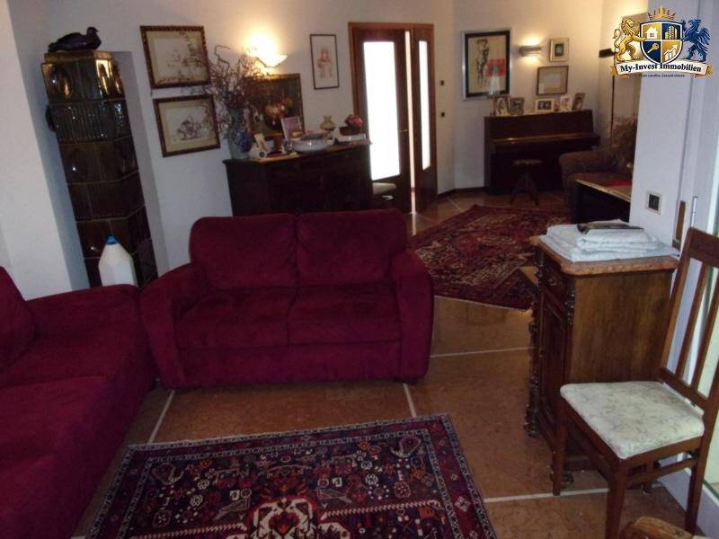 Gemütliches Wohnzimmer mit bequemen roten Sofas, orientalischen Teppichen und einem Kachelofen.