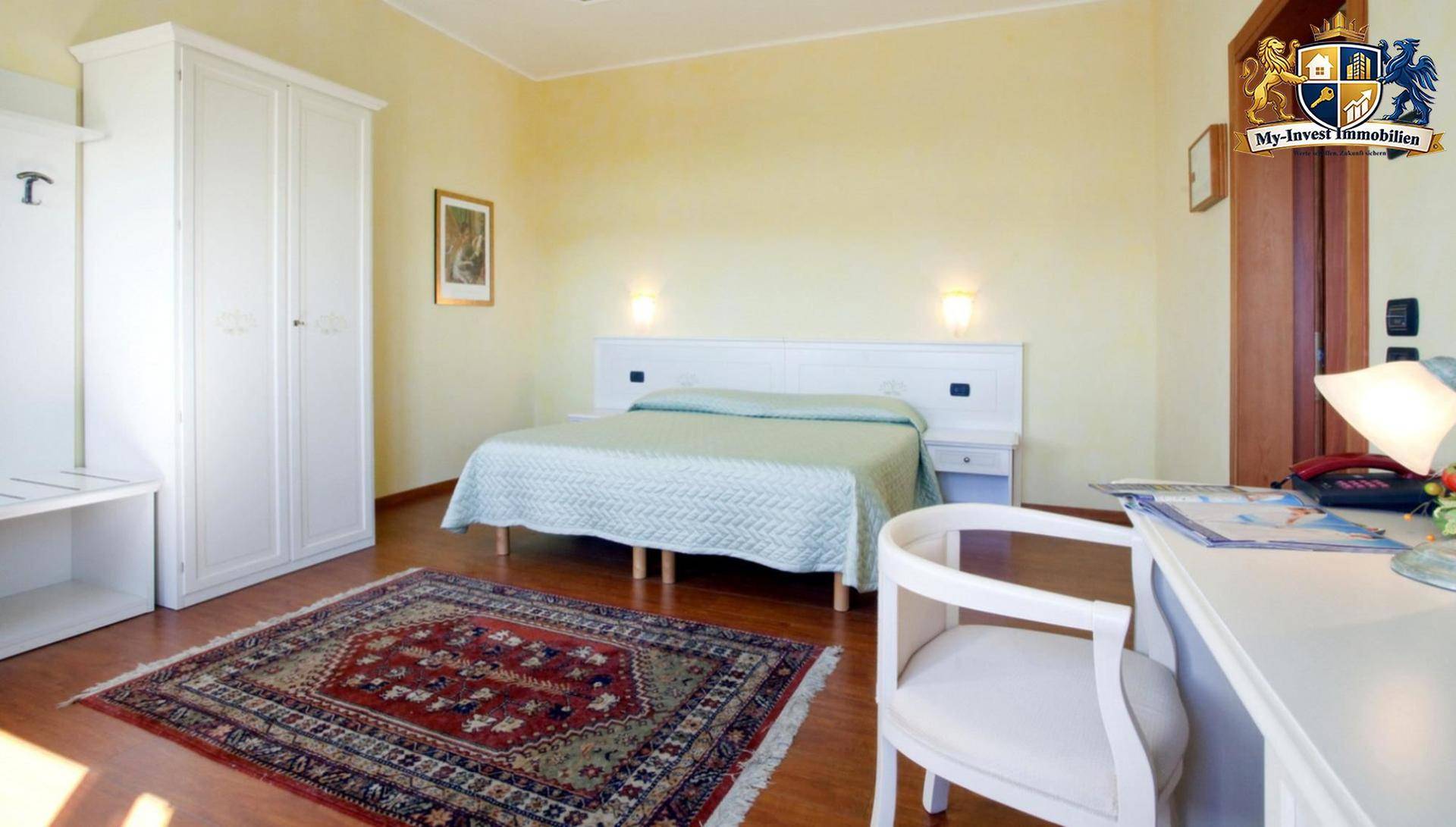 Helles Schlafzimmer mit Doppelbett, weißem Kleiderschrank und Schreibtisch, auf Holzboden.