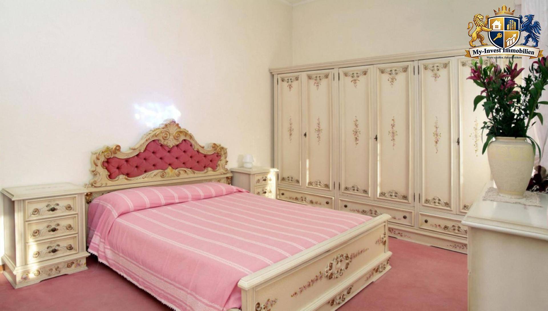 Klassisches Schlafzimmer mit rosa Bettwäsche, verzierten Möbeln und einem großen Kleiderschrank.