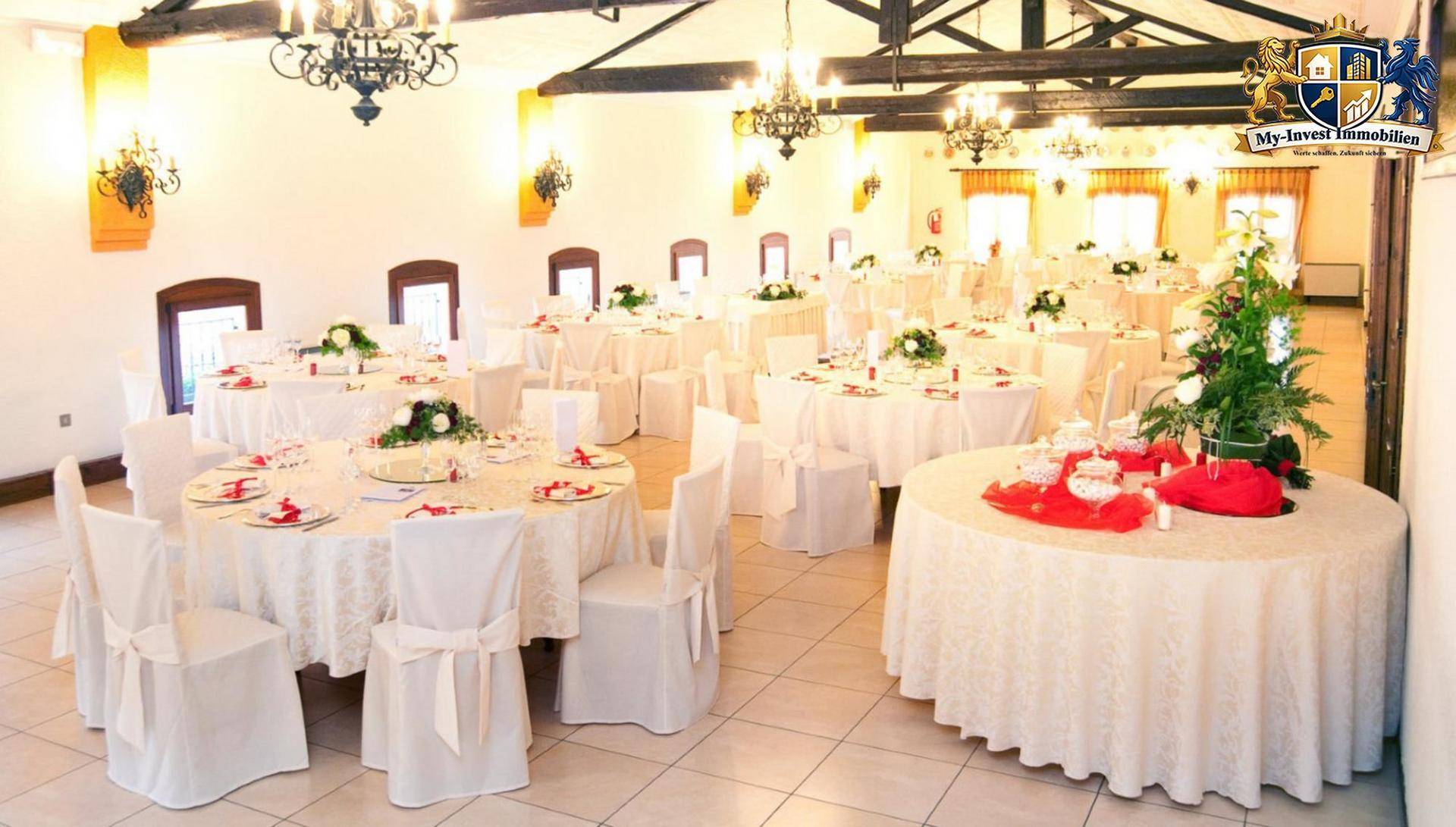 Großer, festlich gedeckter Speisesaal mit vielen runden Tischen, weißen Stühlen und eleganten Kronleuchtern.